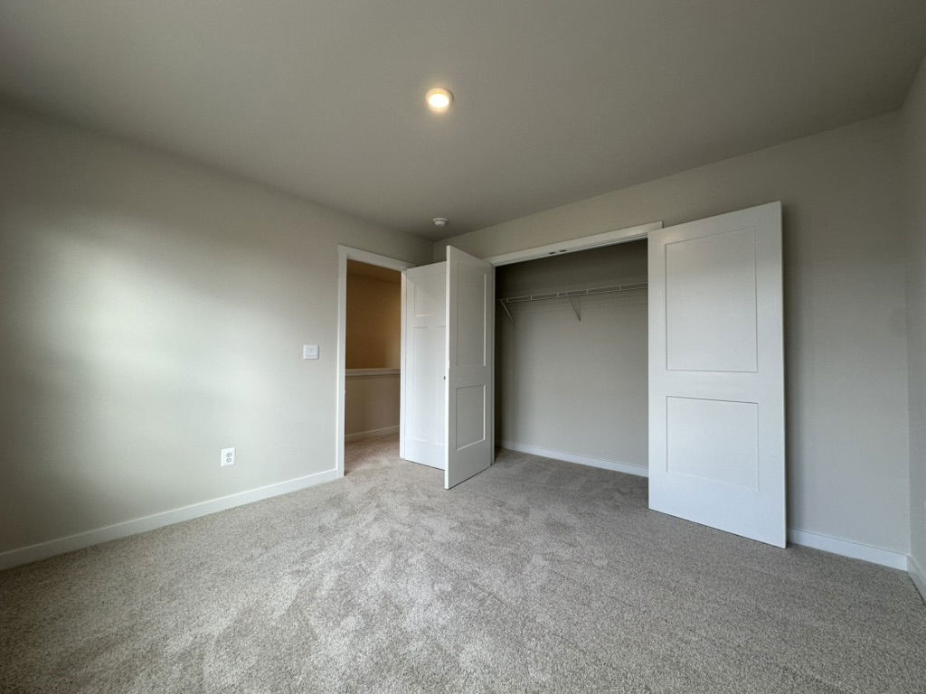Spacious bedroom with carpet flooring and double closet doors open to a well-lit interior.