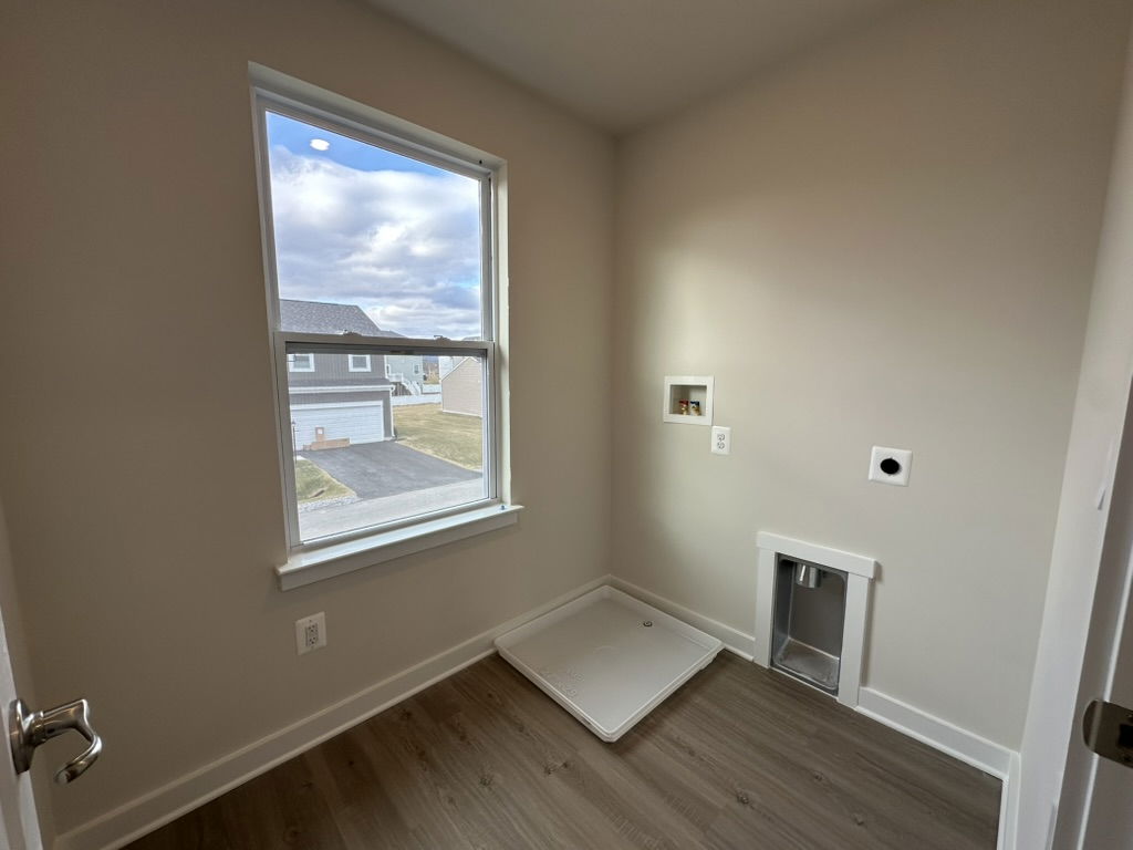 Bright and empty laundry room with a window and dog door, featuring light-colored walls and wooden flooring.