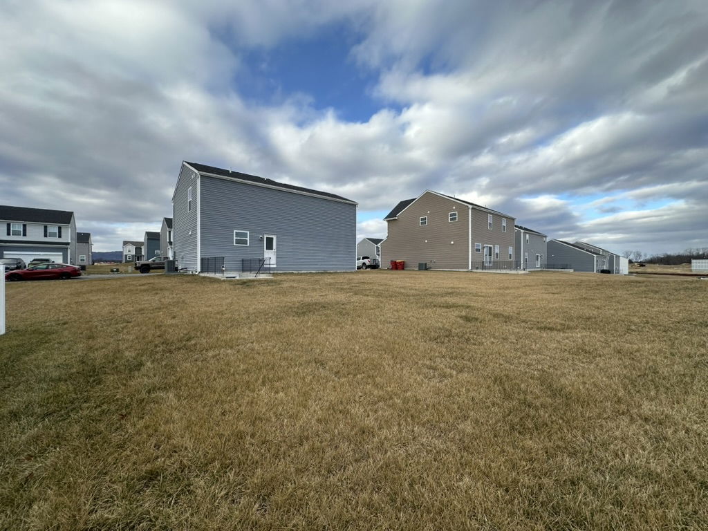 A view of residential houses in a suburban neighborhood with cloudy skies and tall grass in the foreground.
