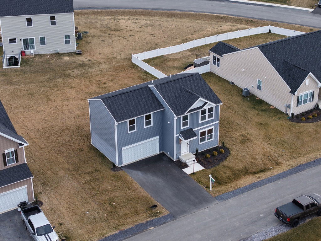 Aerial view of a modern grey house with a driveway in a suburban neighborhood featuring manicured lawns and neighboring homes.