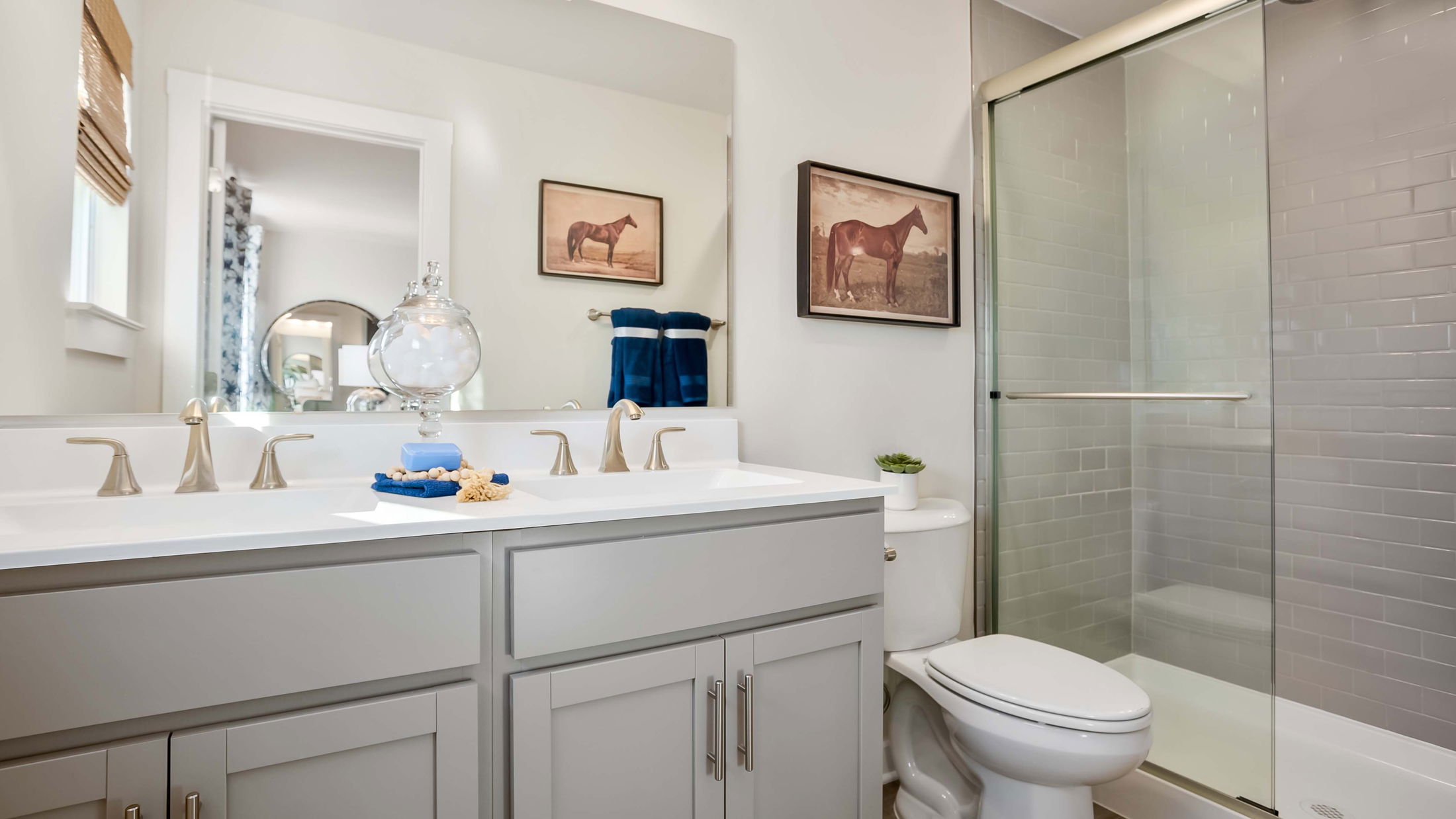 Modern bathroom with glass shower, double vanity, and horse-themed wall art.