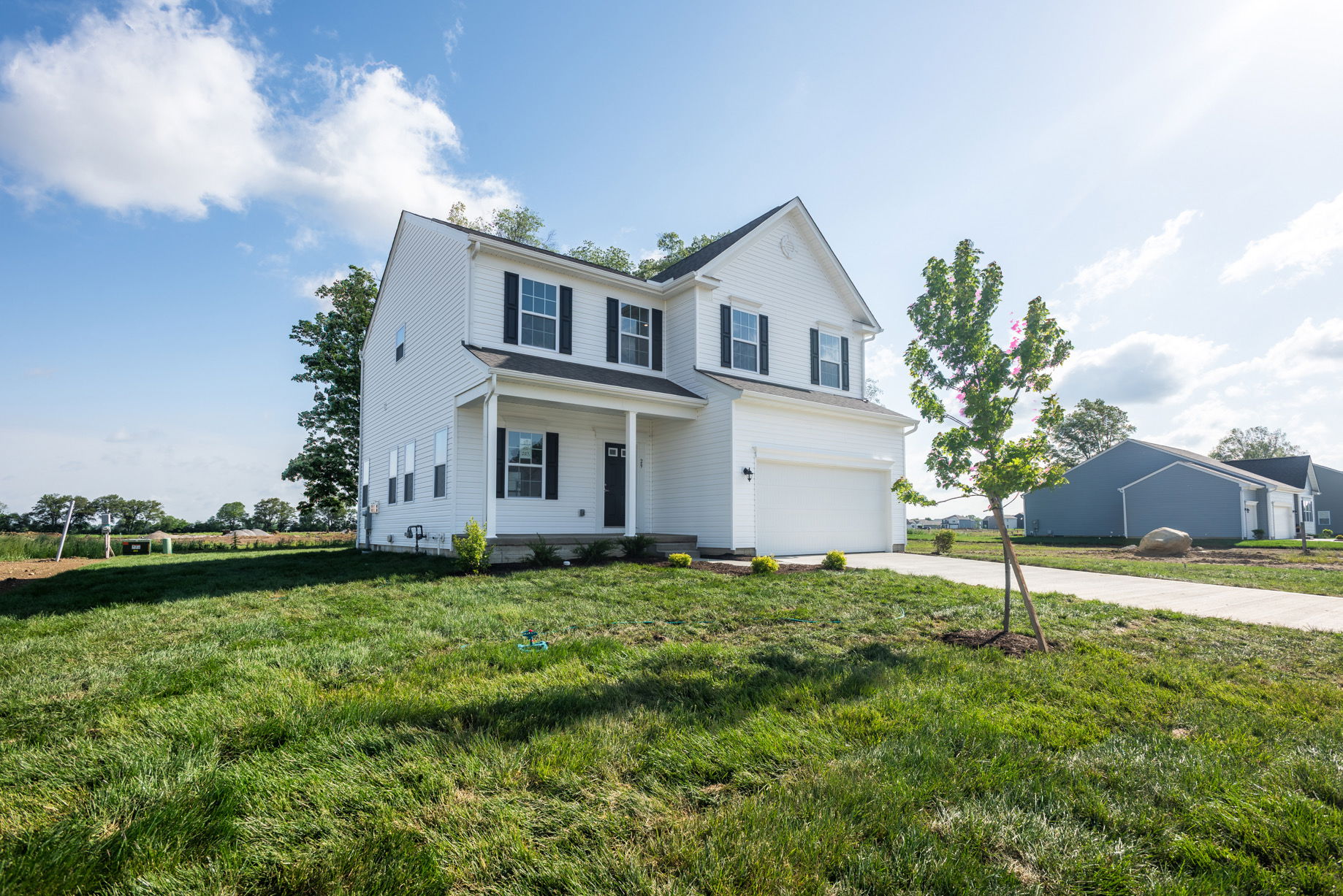 Two-story white suburban house with a manicured lawn, garage, and clear blue sky.