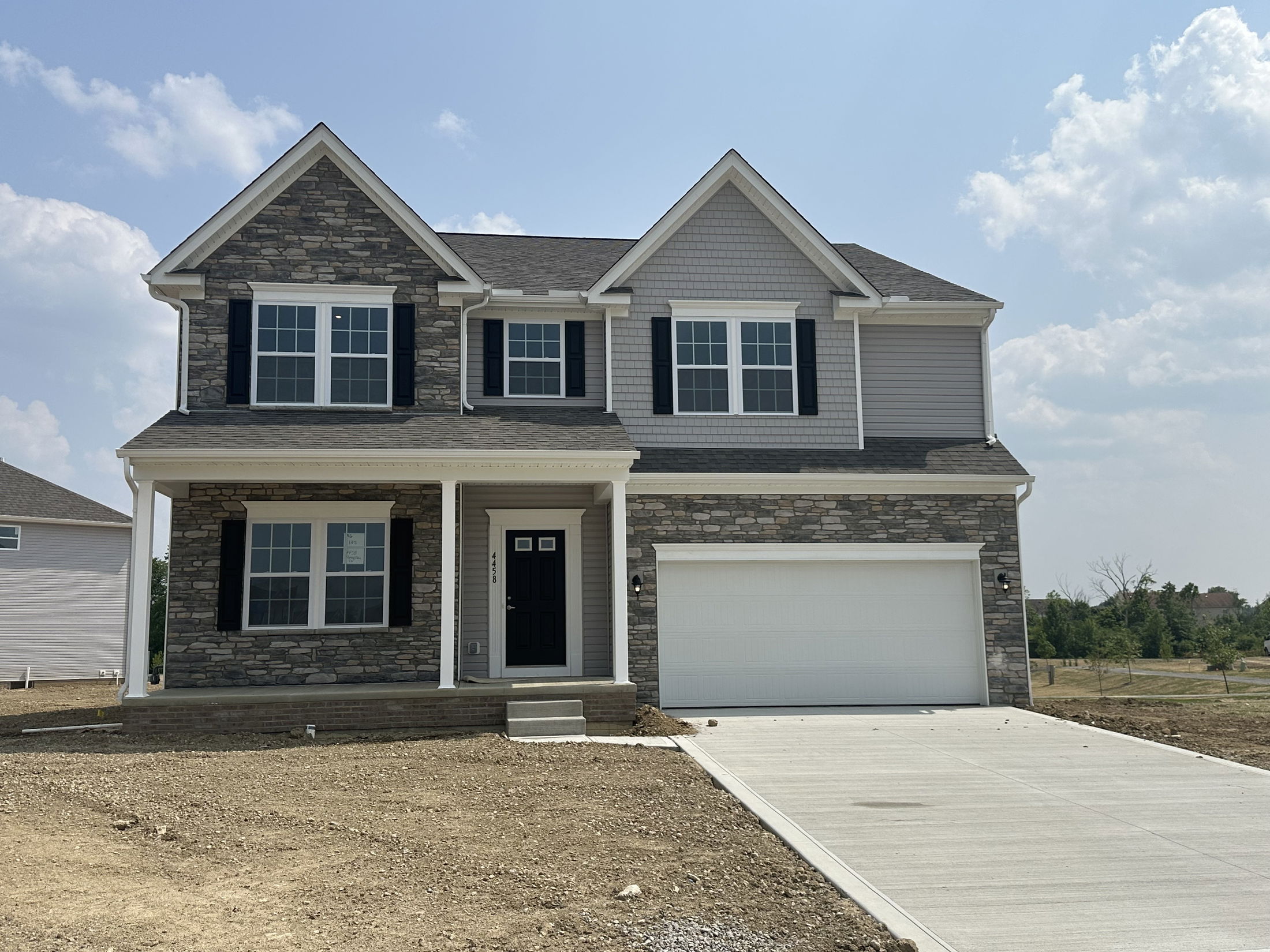 Newly constructed two-story house with stone facade, black shutters, and attached garage on a sunny day.