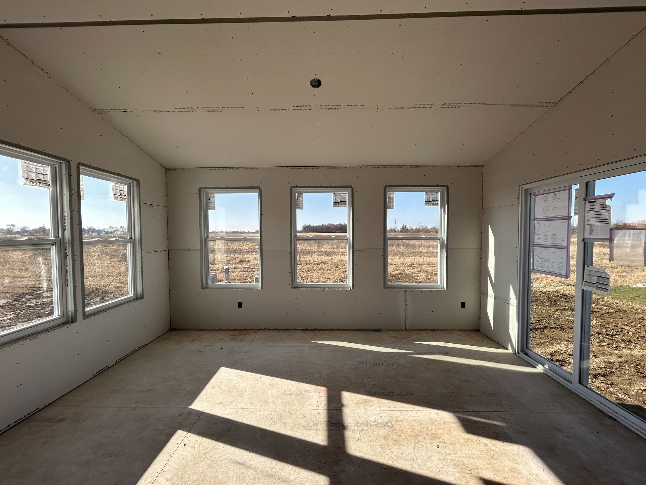 Interior view of a partially constructed room with multiple windows overlooking a rural landscape.