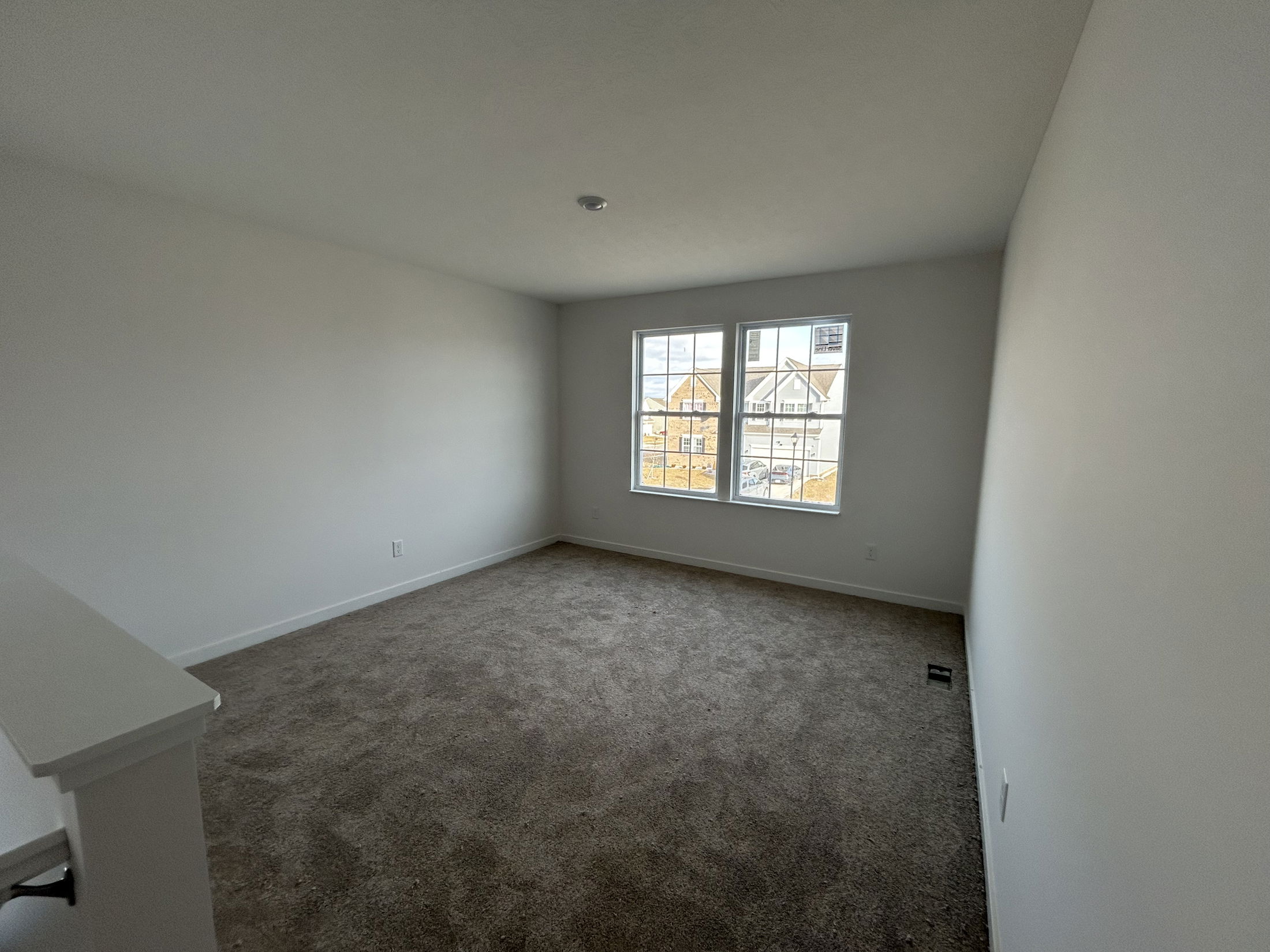 Spacious and well-lit living room with large windows and neutral carpet, perfect for modern living.