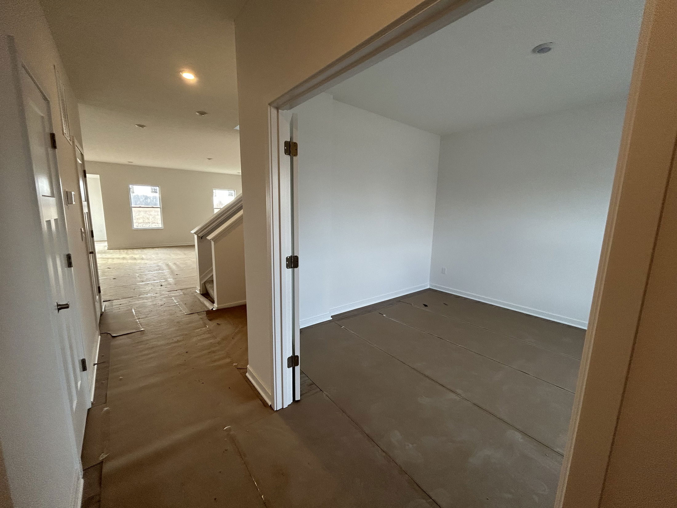A spacious empty hallway leads to a light-filled room in a newly constructed home.