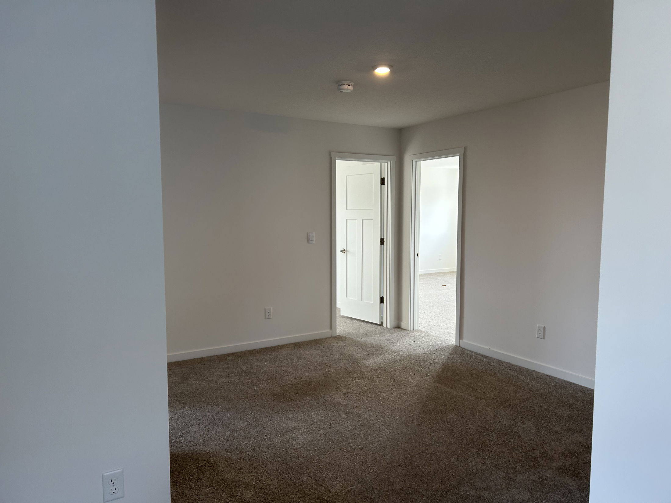 Spacious, well-lit interior of a modern room featuring beige carpet and white walls with doorways leading to adjacent spaces.