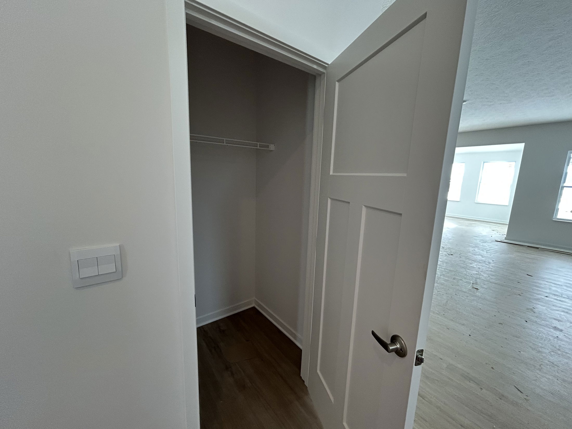 A spacious closet is partially open, showcasing a clean interior and modern door design in a newly constructed room.