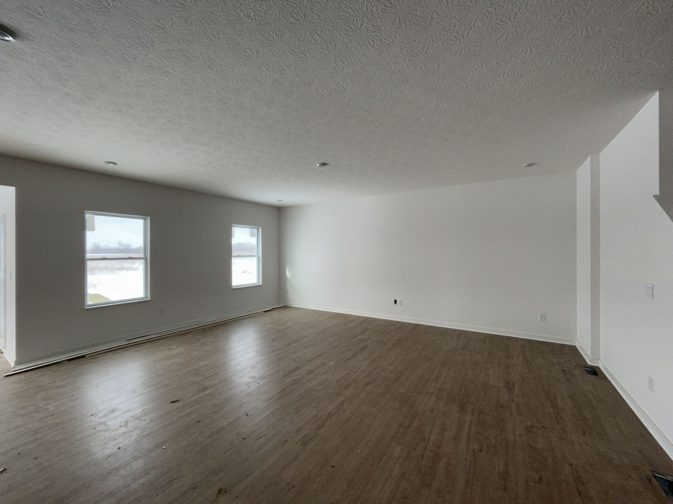 Spacious, empty living room with natural light from large windows and modern laminate flooring.