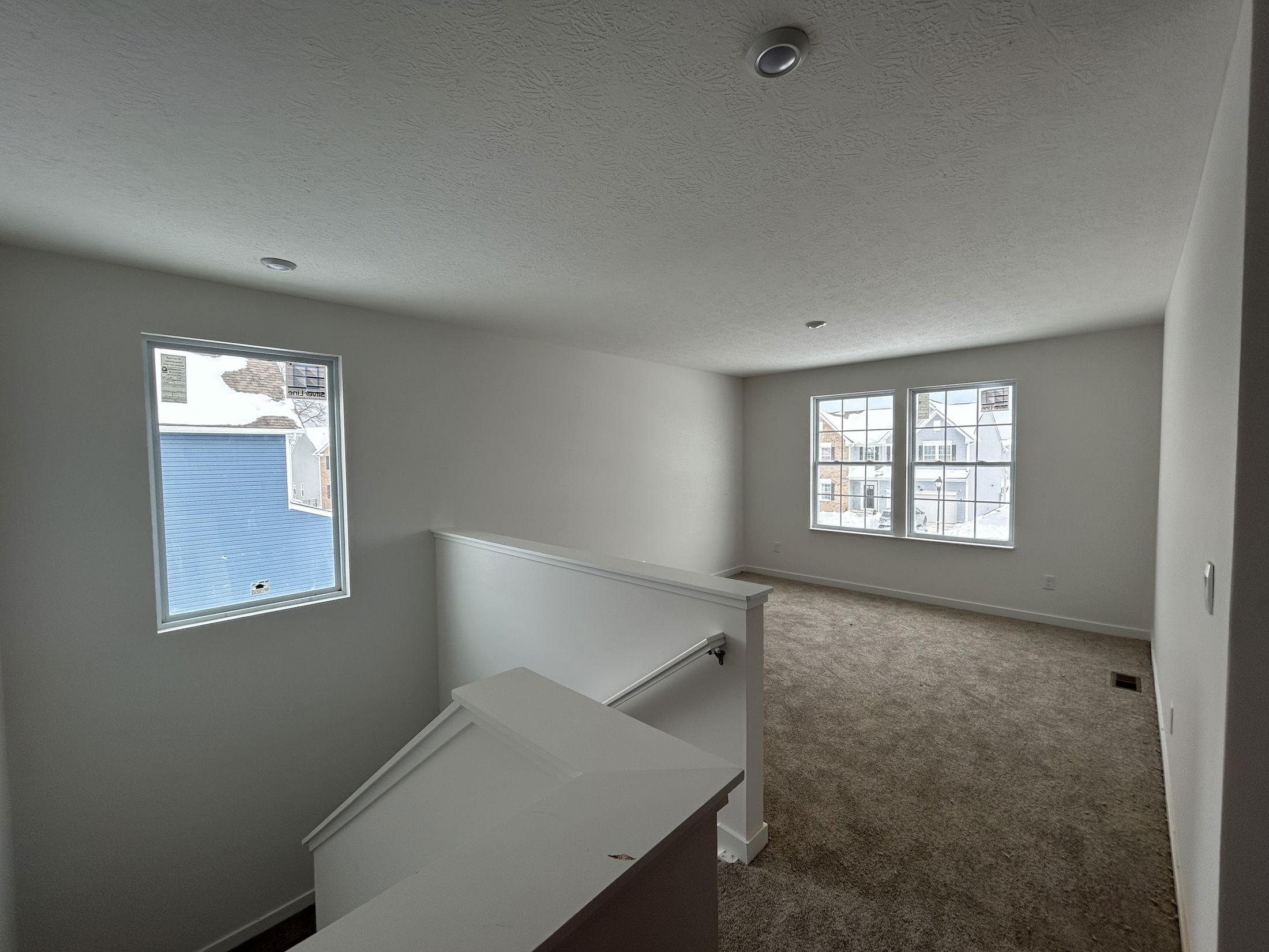 Bright and airy living space featuring large windows, carpeted flooring, and neutral-colored walls.