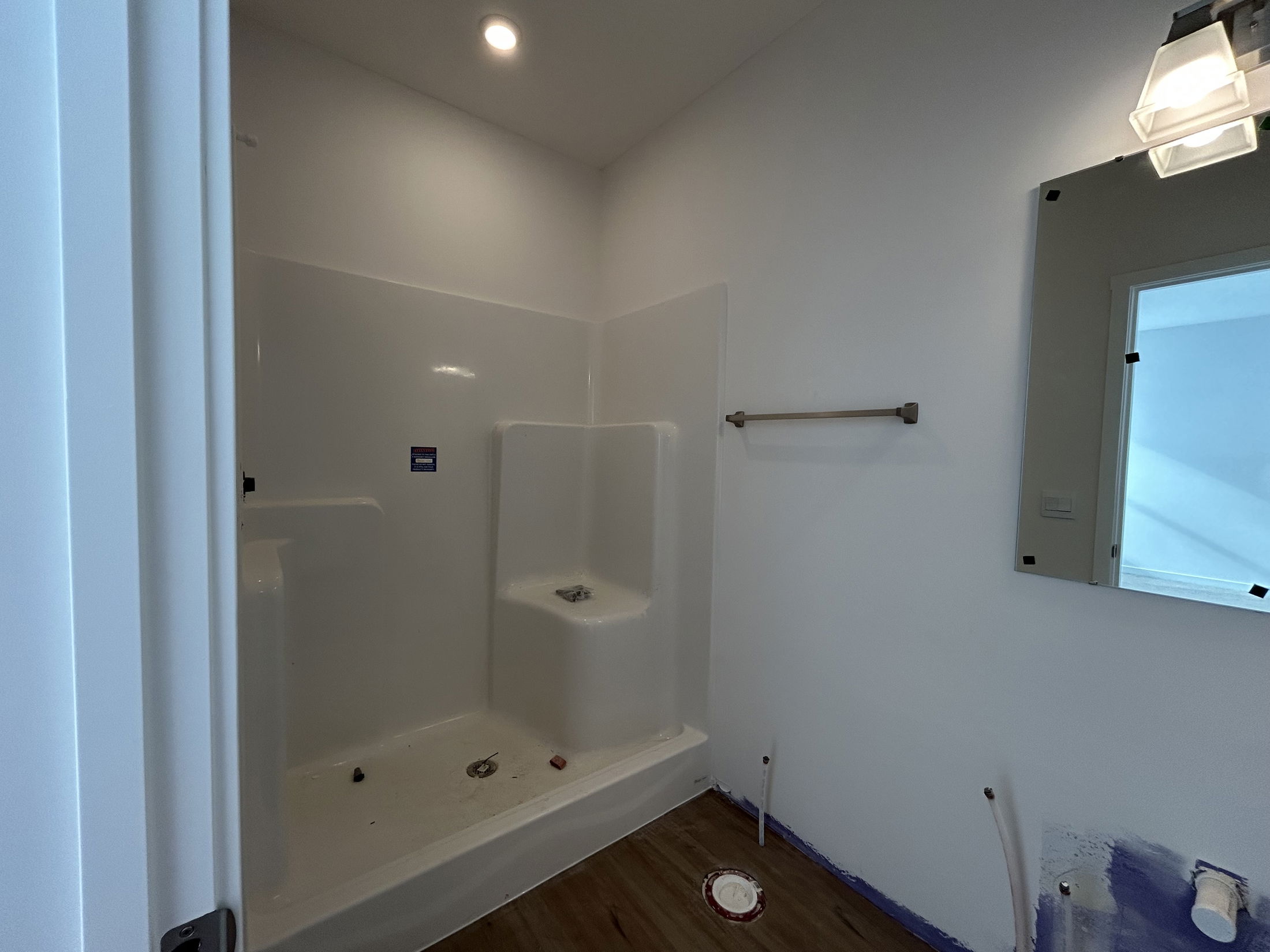 Modern bathroom renovation featuring a white shower stall, unfinished walls, and a simple mirror with natural lighting.