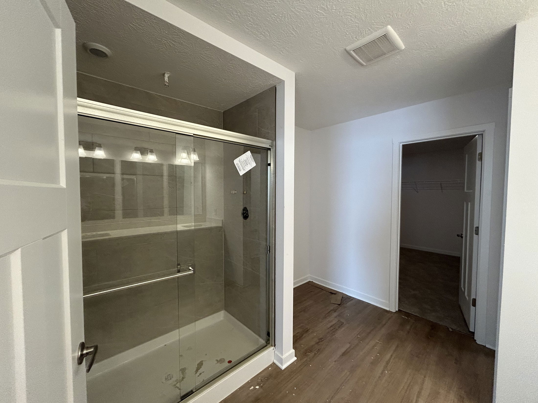 Modern bathroom featuring a glass shower enclosure, new lighting fixtures, and spacious light-colored walls.