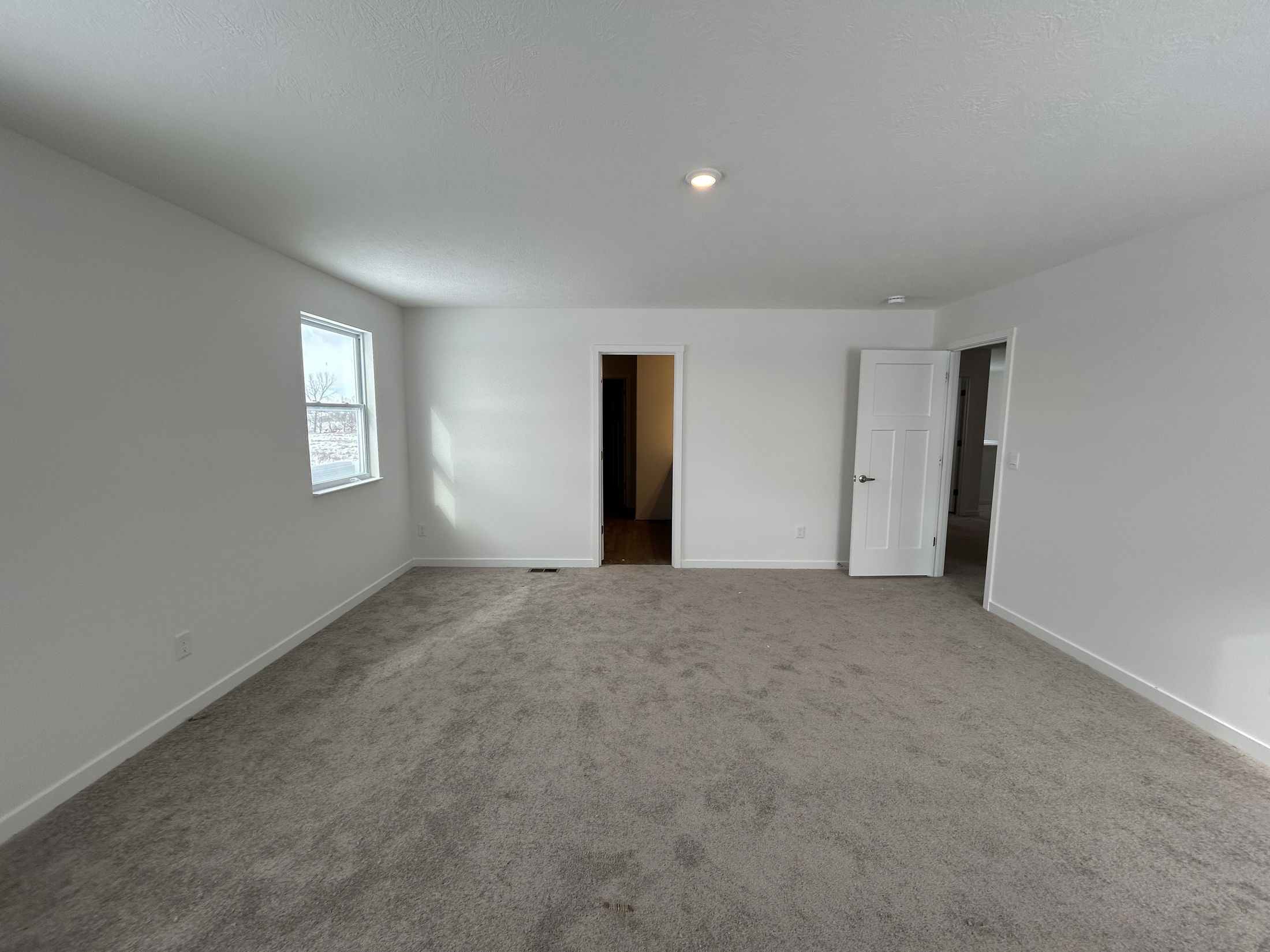 Spacious living room with light gray carpet, white walls, and large windows creating a bright atmosphere.