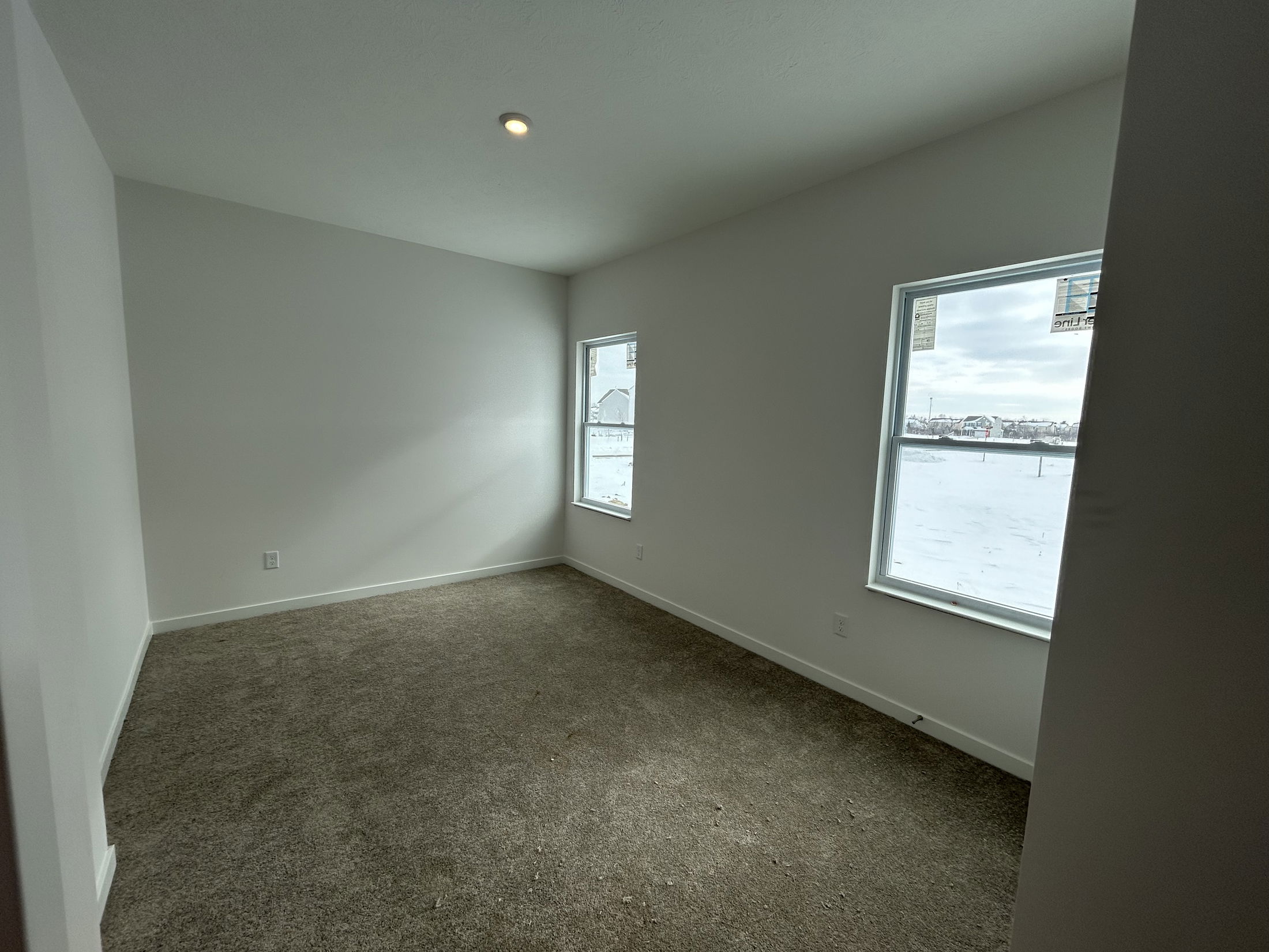 A bright, empty room with large windows showcasing a winter landscape and beige carpet flooring.