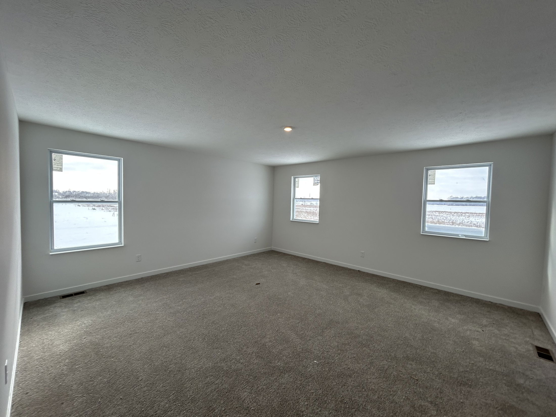 Spacious, empty living room with large windows offering natural light and a view of the snowy landscape outside.