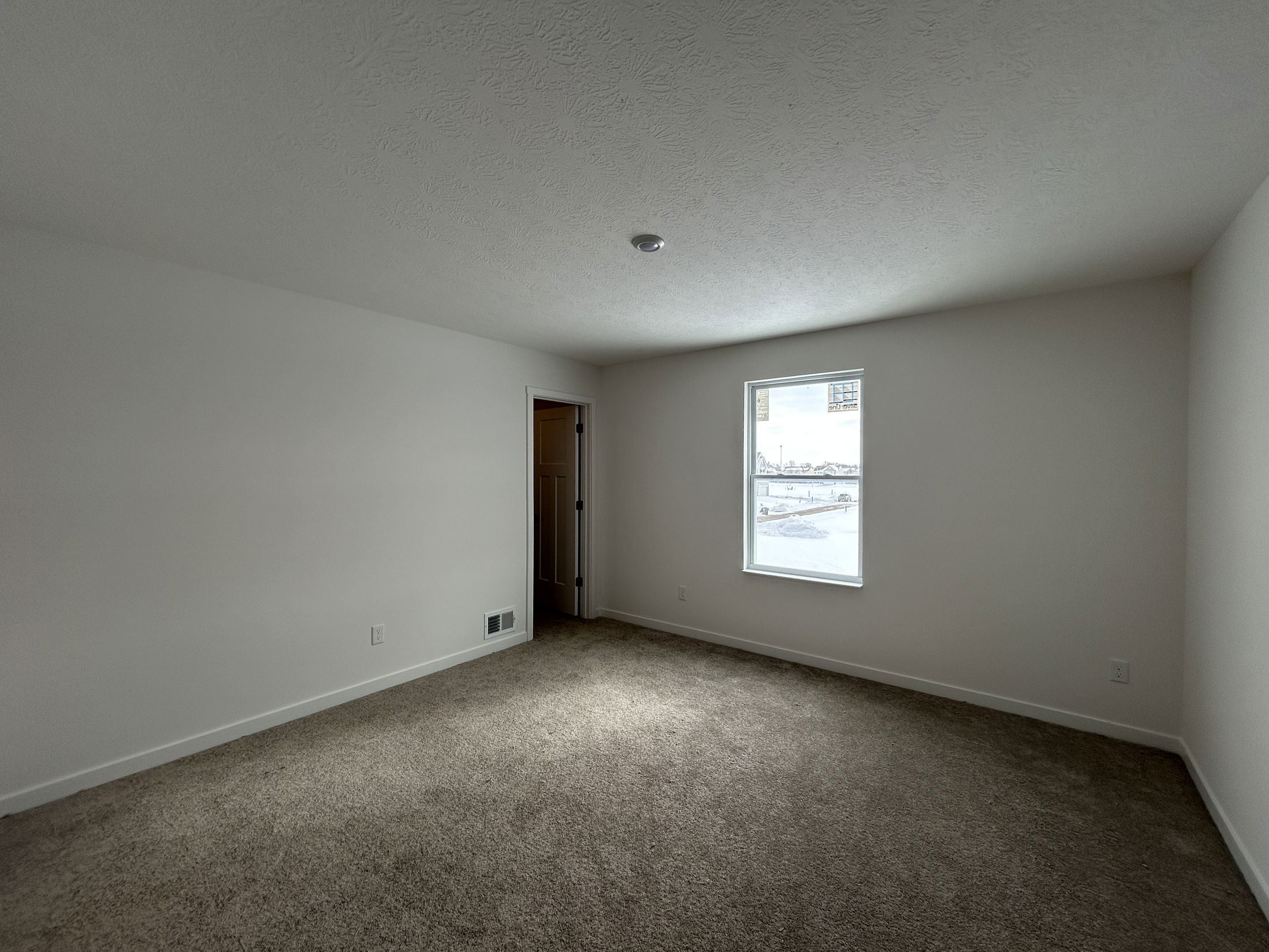 Spacious empty bedroom with carpeted flooring, white walls, and a large window allowing natural light.