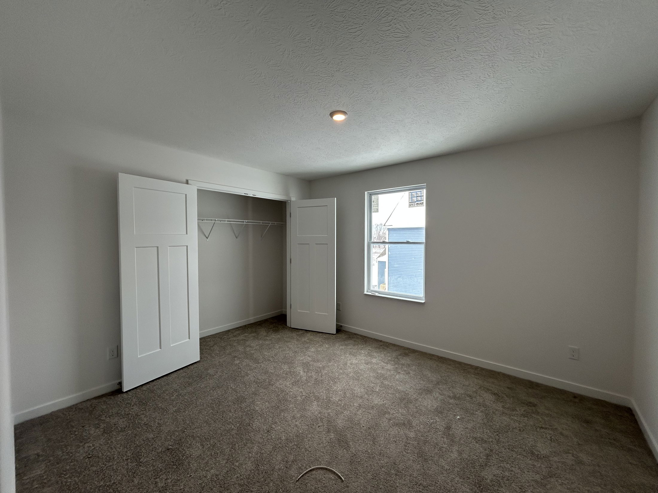 Spacious and well-lit bedroom with beige carpet, closet with sliding doors, and a window overlooking the outside.