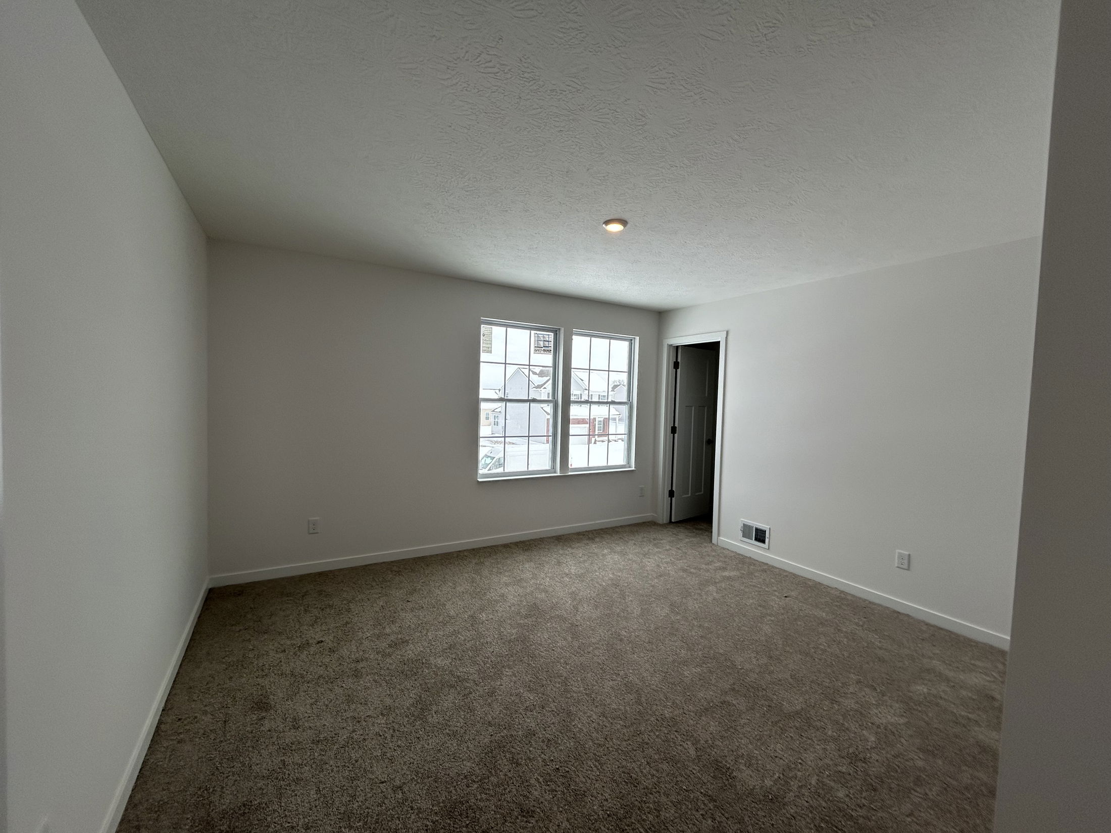 Spacious living room with beige carpet and large window providing natural light, showcasing a minimalist design.