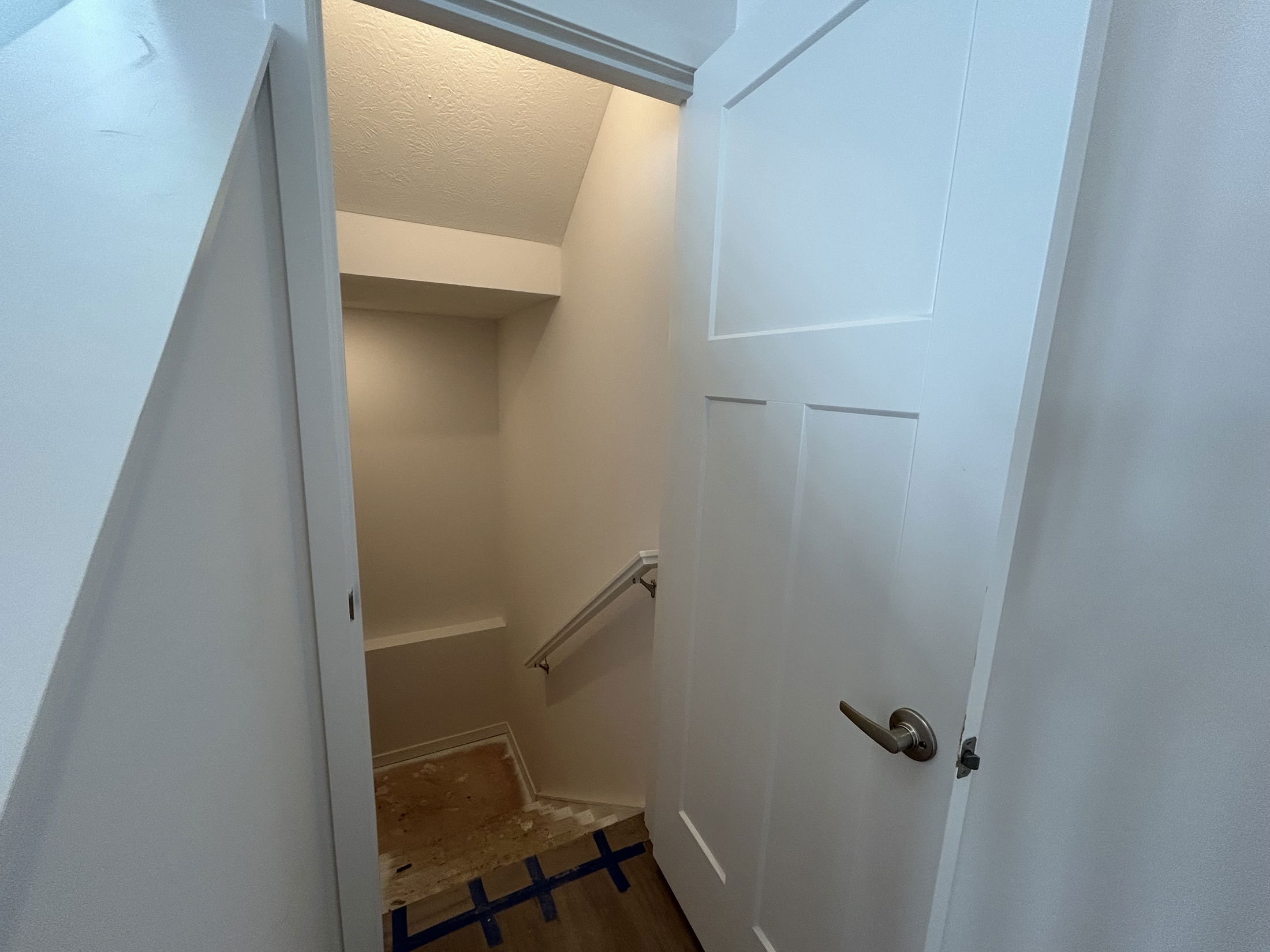 Interior view of a stairway leading down from a white door, featuring a lighted wall and wooden flooring.