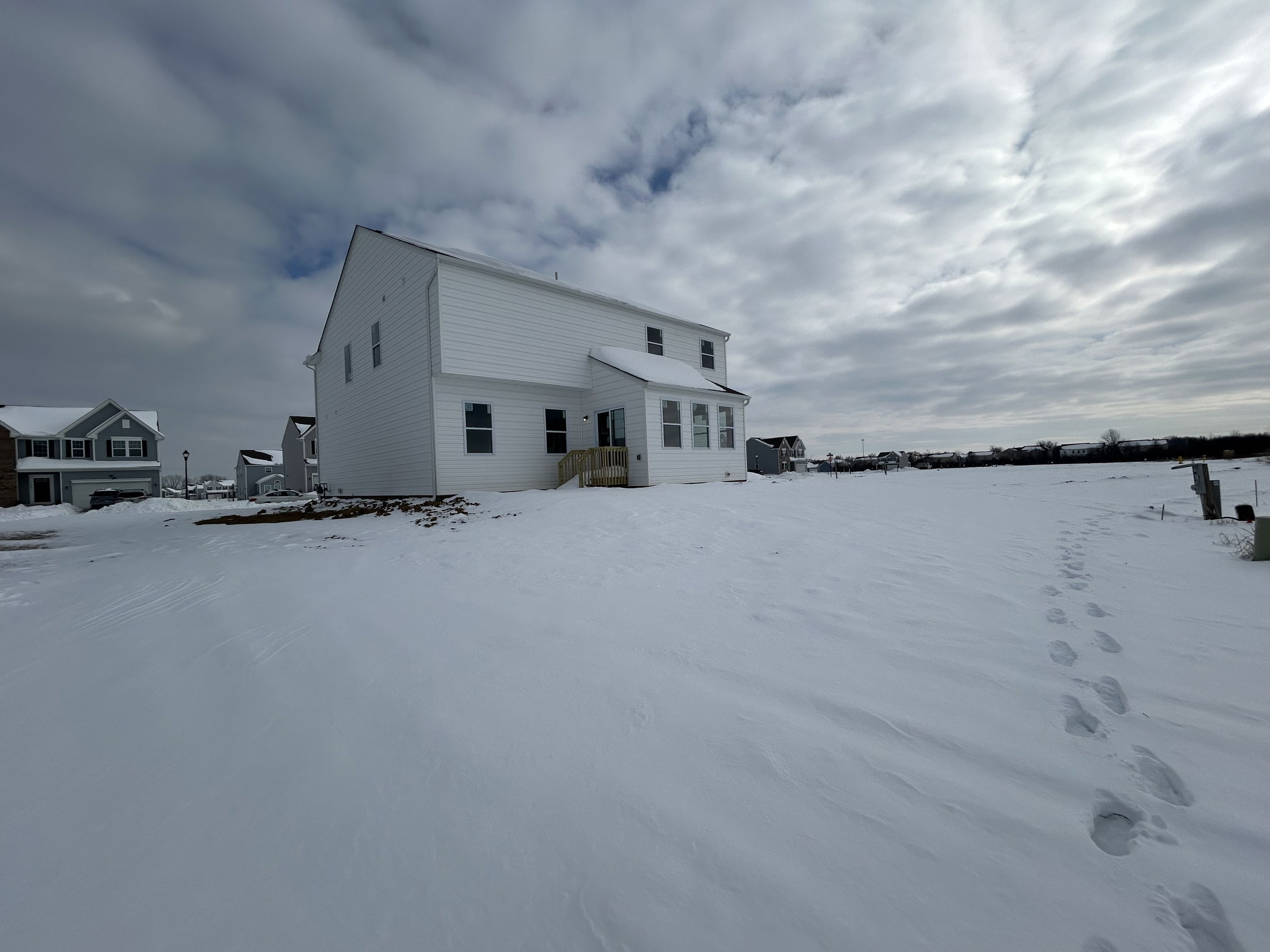 Modern two-story house in a snowy neighborhood under cloudy skies.