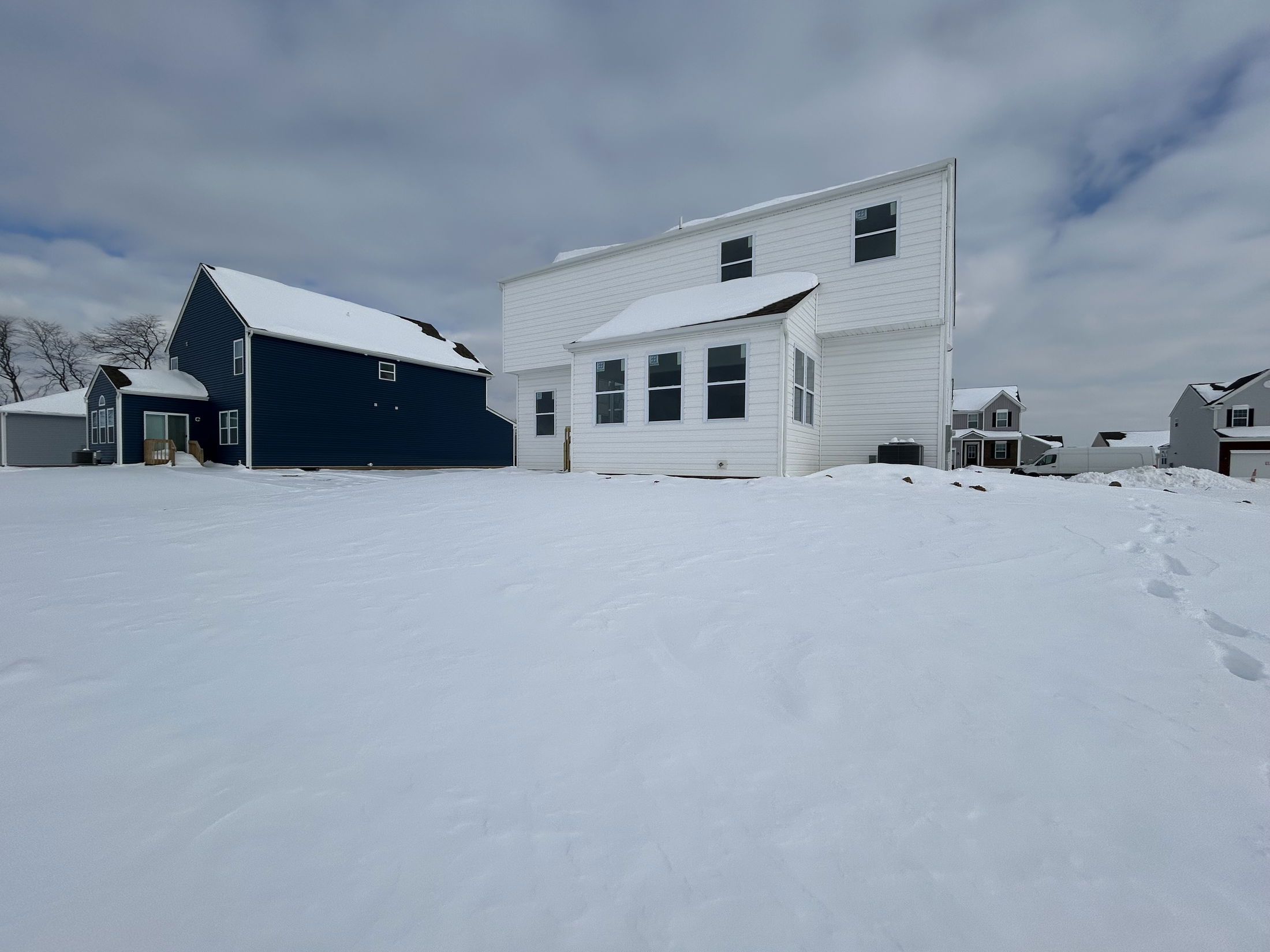 A snowy winter scene showing two houses, one blue and one white, with a cloudy sky in the background.