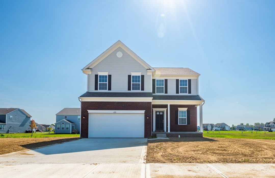 Newly constructed two-story suburban home with a spacious front driveway under a clear blue sky.