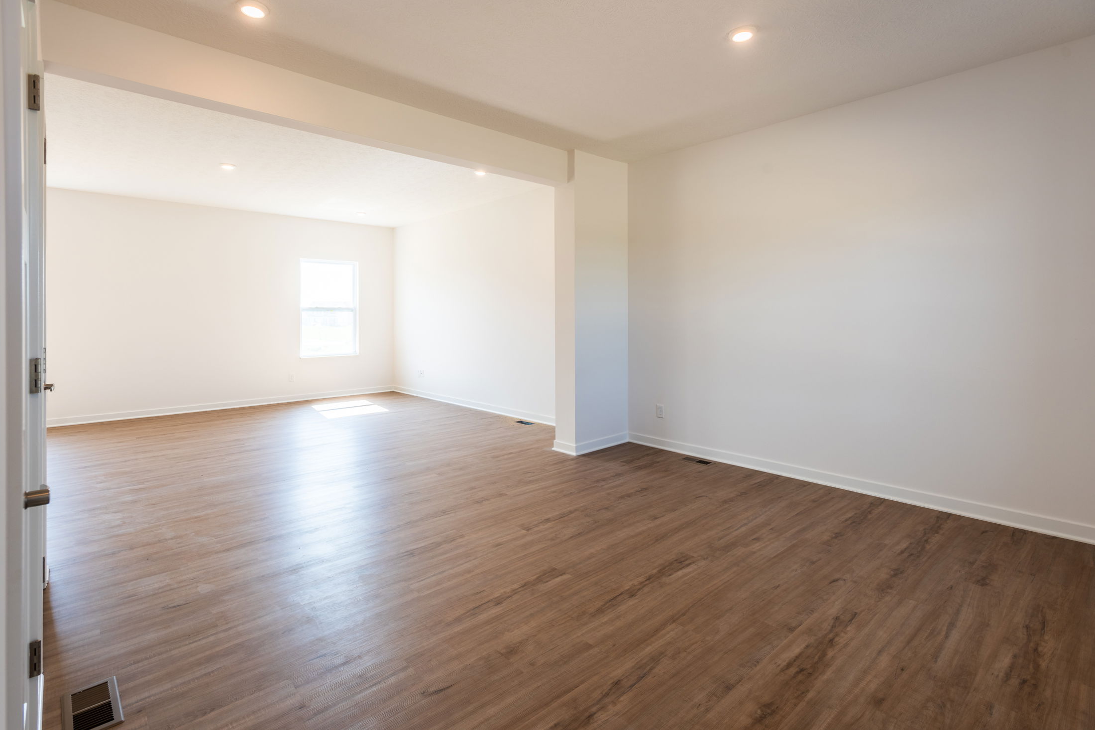 Empty room with smooth wooden floors, white walls, and recessed lighting, showcasing a bright and airy interior design.