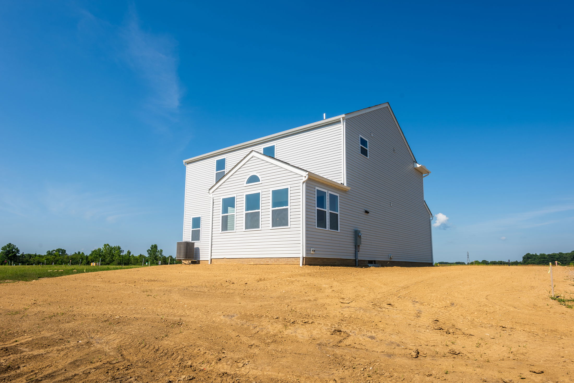 Newly constructed white house on a bare dirt plot under a clear blue sky.