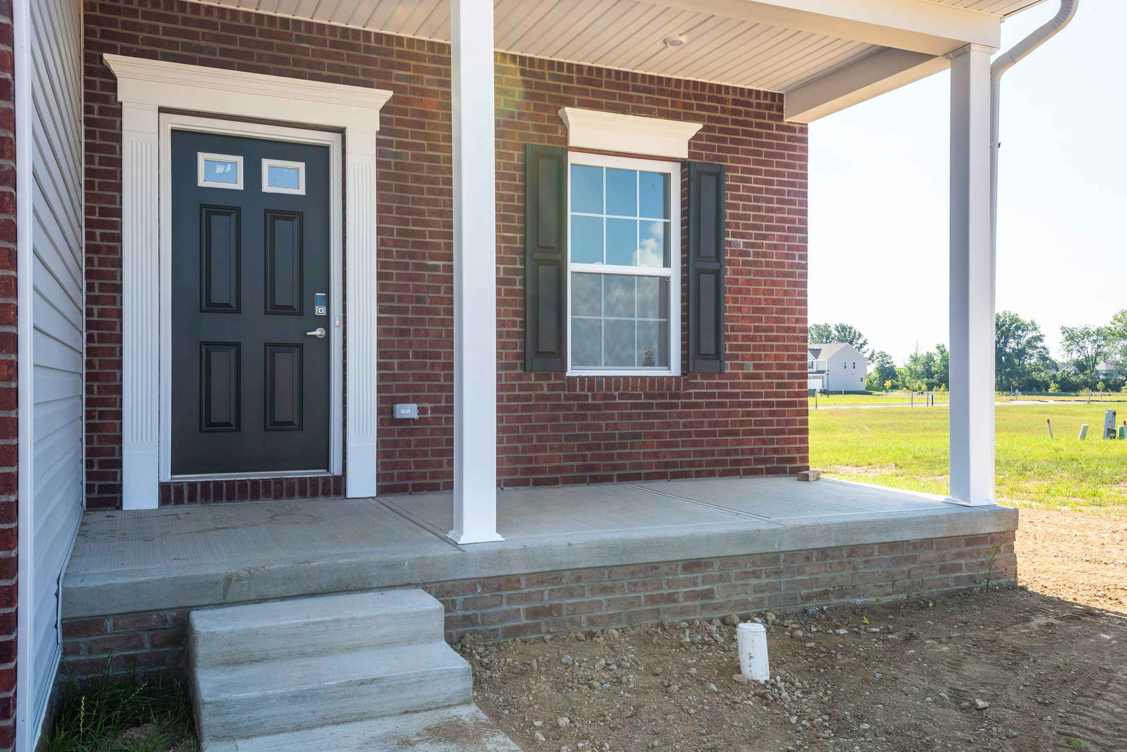 Front entrance of a modern red brick house with a black door and large window on a concrete porch.