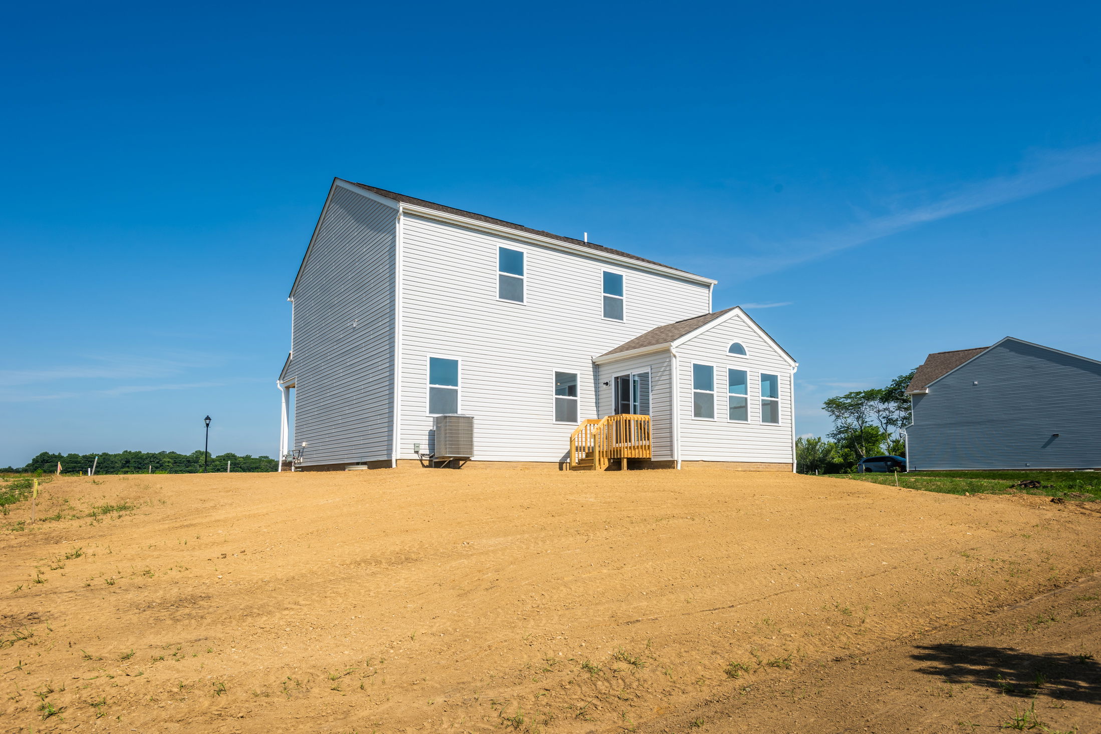 Newly constructed two-story white house on a freshly landscaped lot under a clear blue sky.