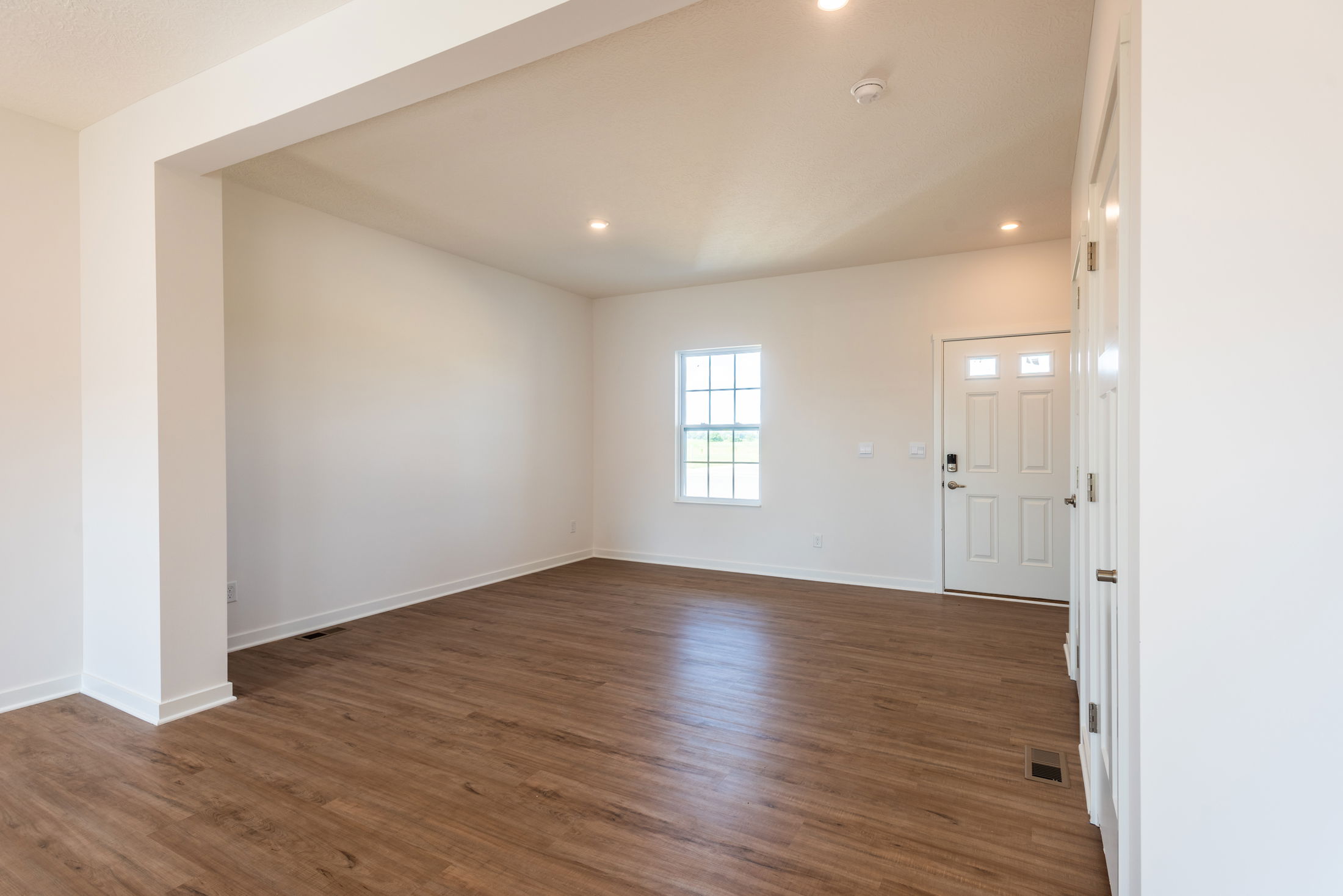 Modern empty room with wooden flooring, white walls, and a door with a window.