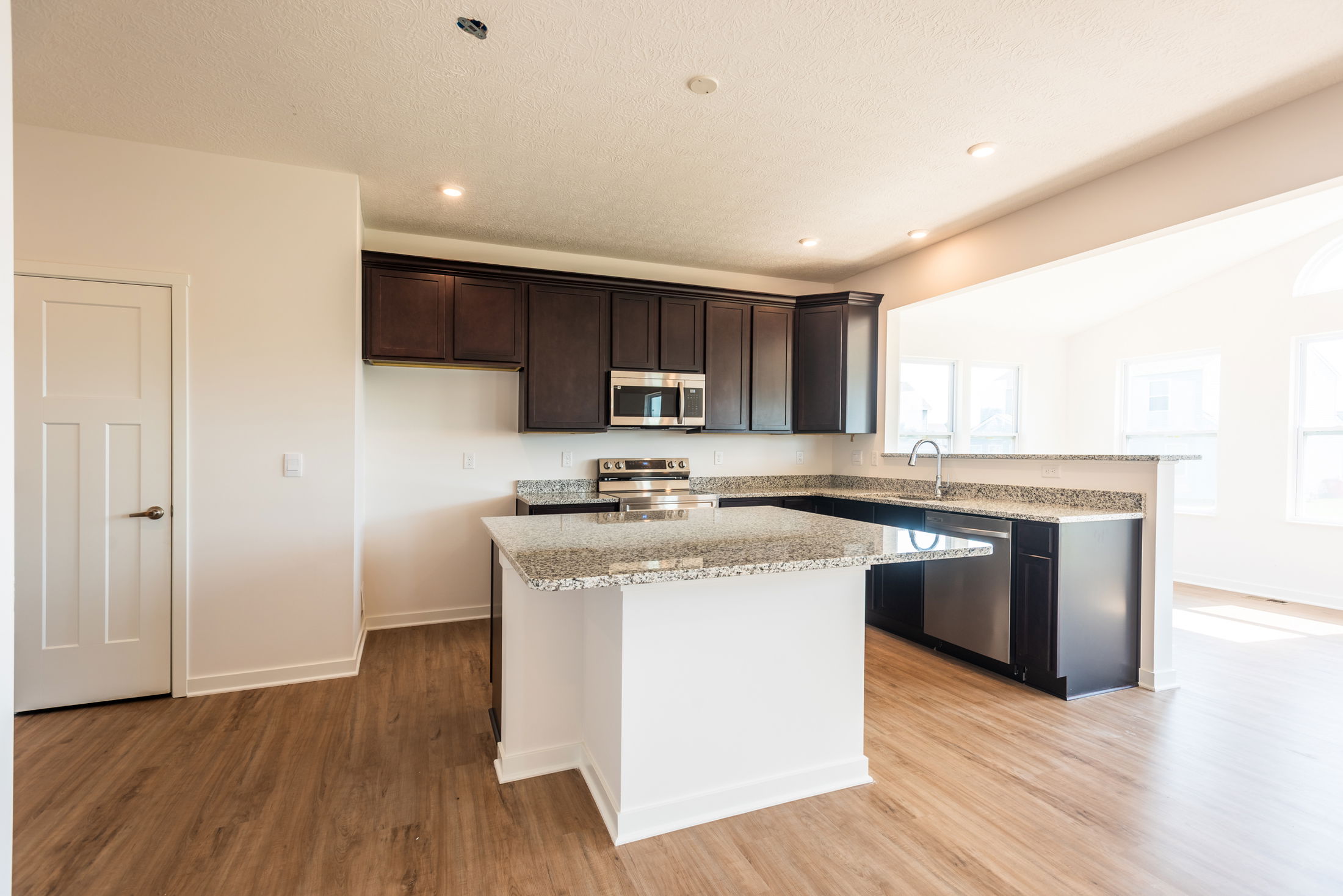 Bright modern kitchen featuring dark wood cabinets, stainless steel appliances, granite countertops, and hardwood flooring.