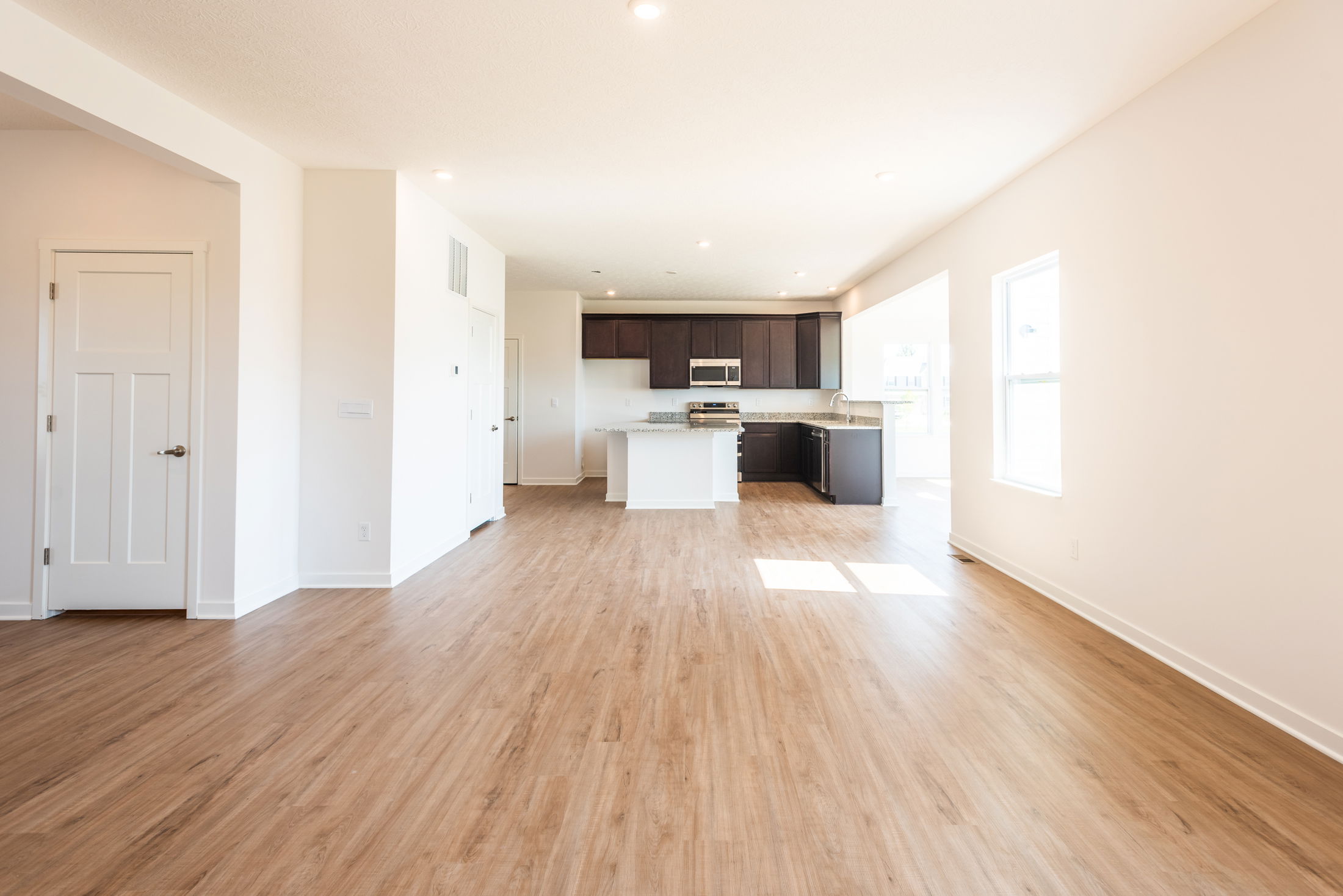 Spacious open-concept living area with light wood flooring, modern kitchen cabinets, and ample natural light.