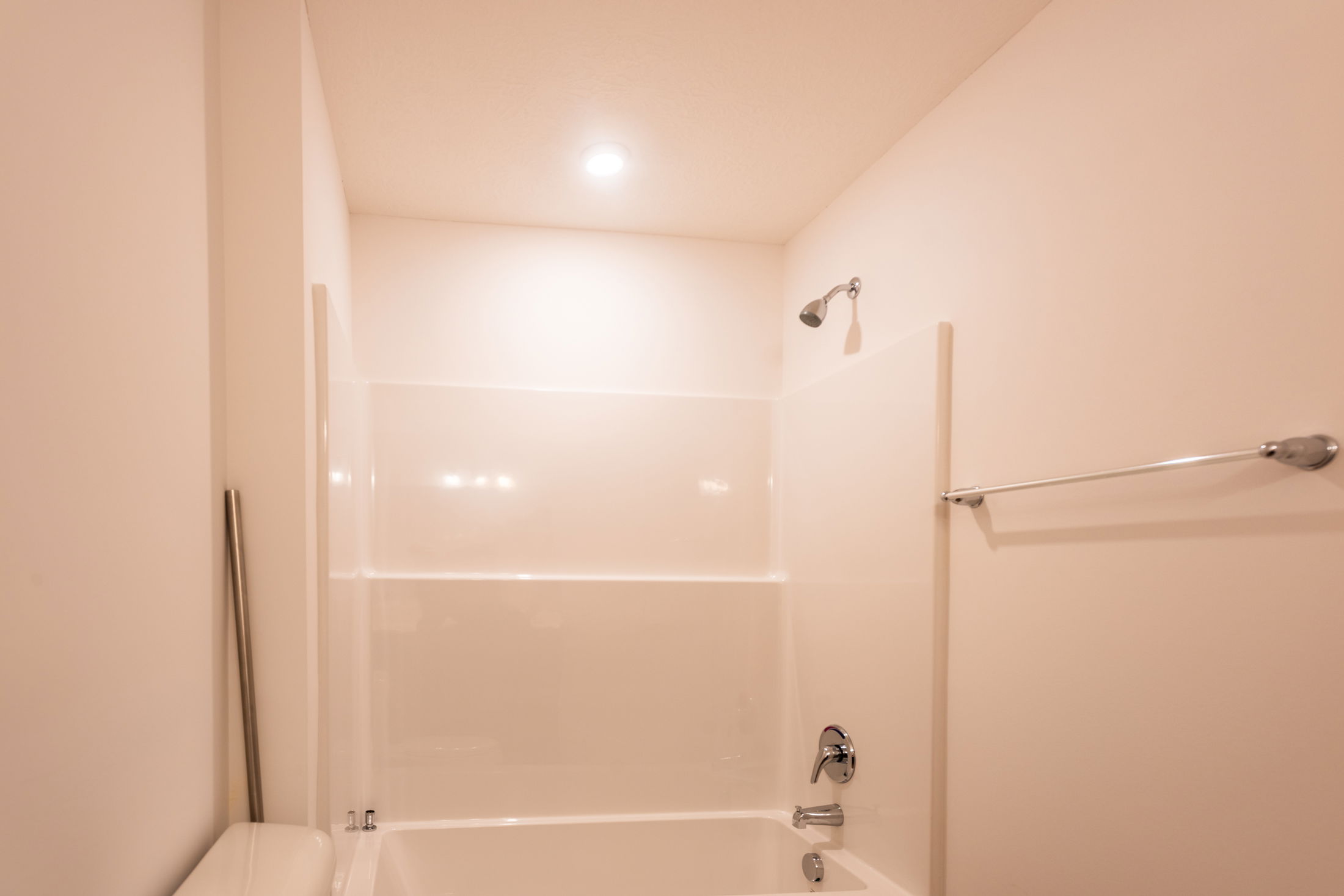 Minimalist bathroom with cream walls featuring a bathtub, showerhead, and towel bar.