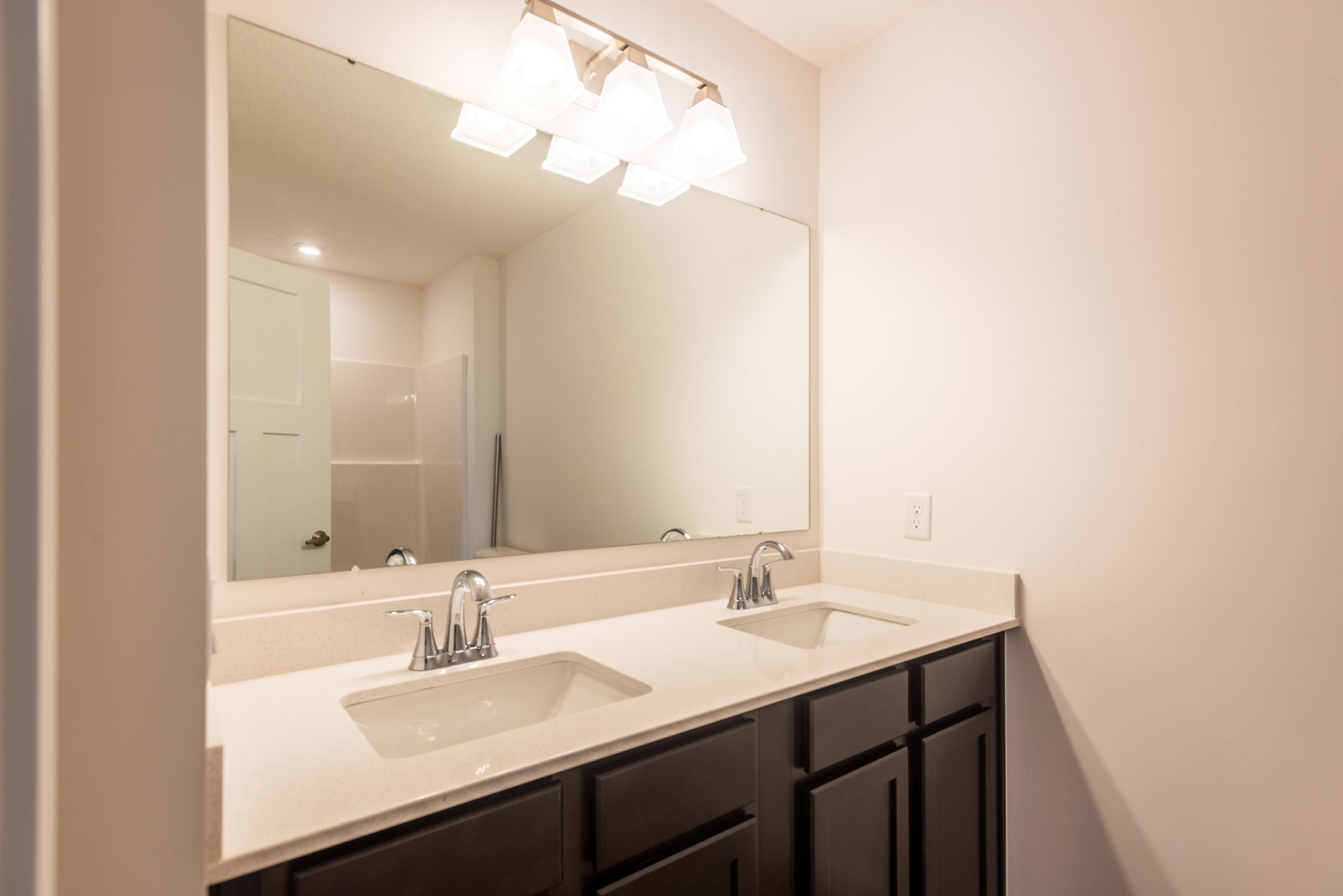 Modern bathroom with a large mirror, dual sinks, and dark wood cabinets under bright overhead lighting.