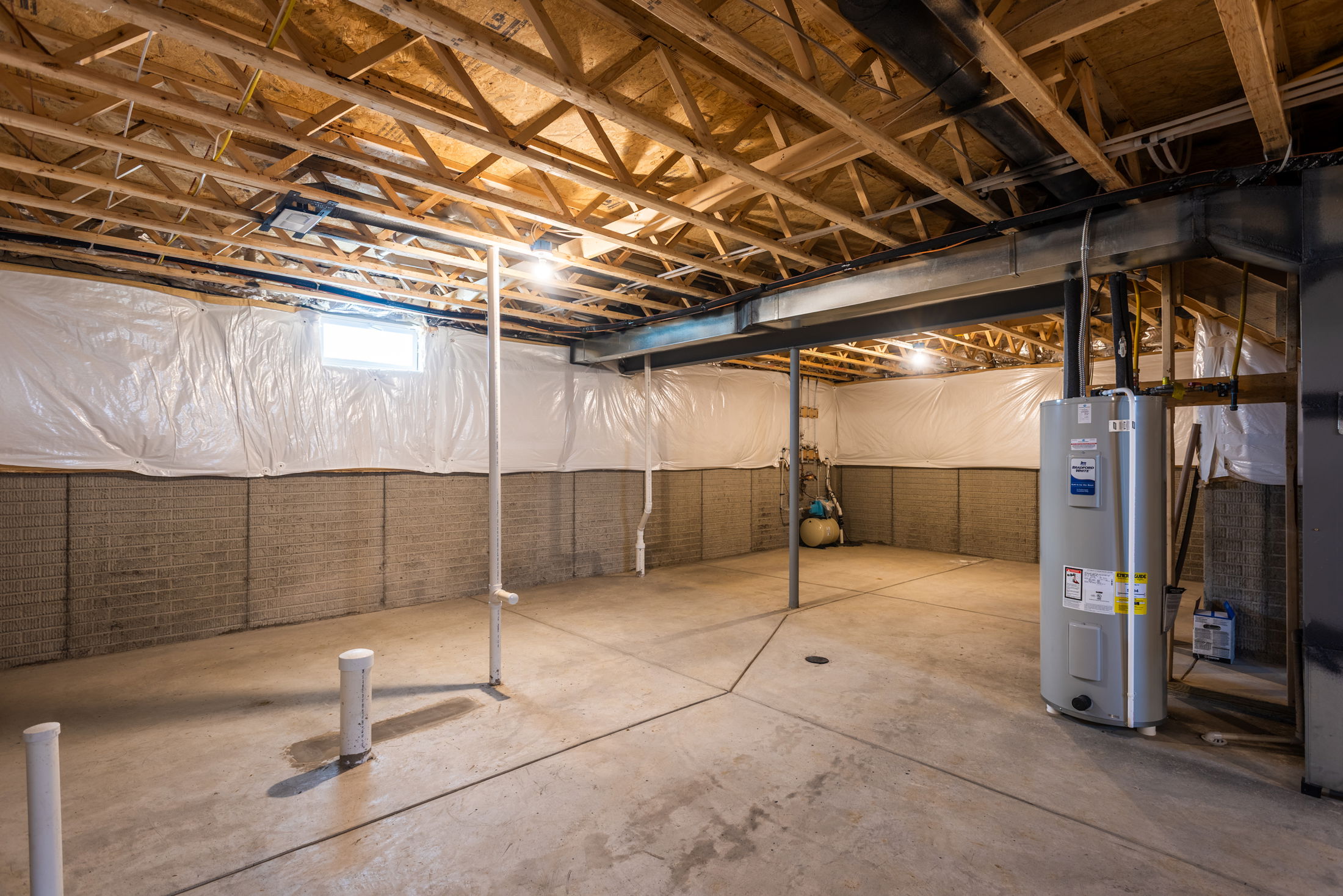 Unfinished basement with exposed wooden beams, concrete floor, and a water heater.