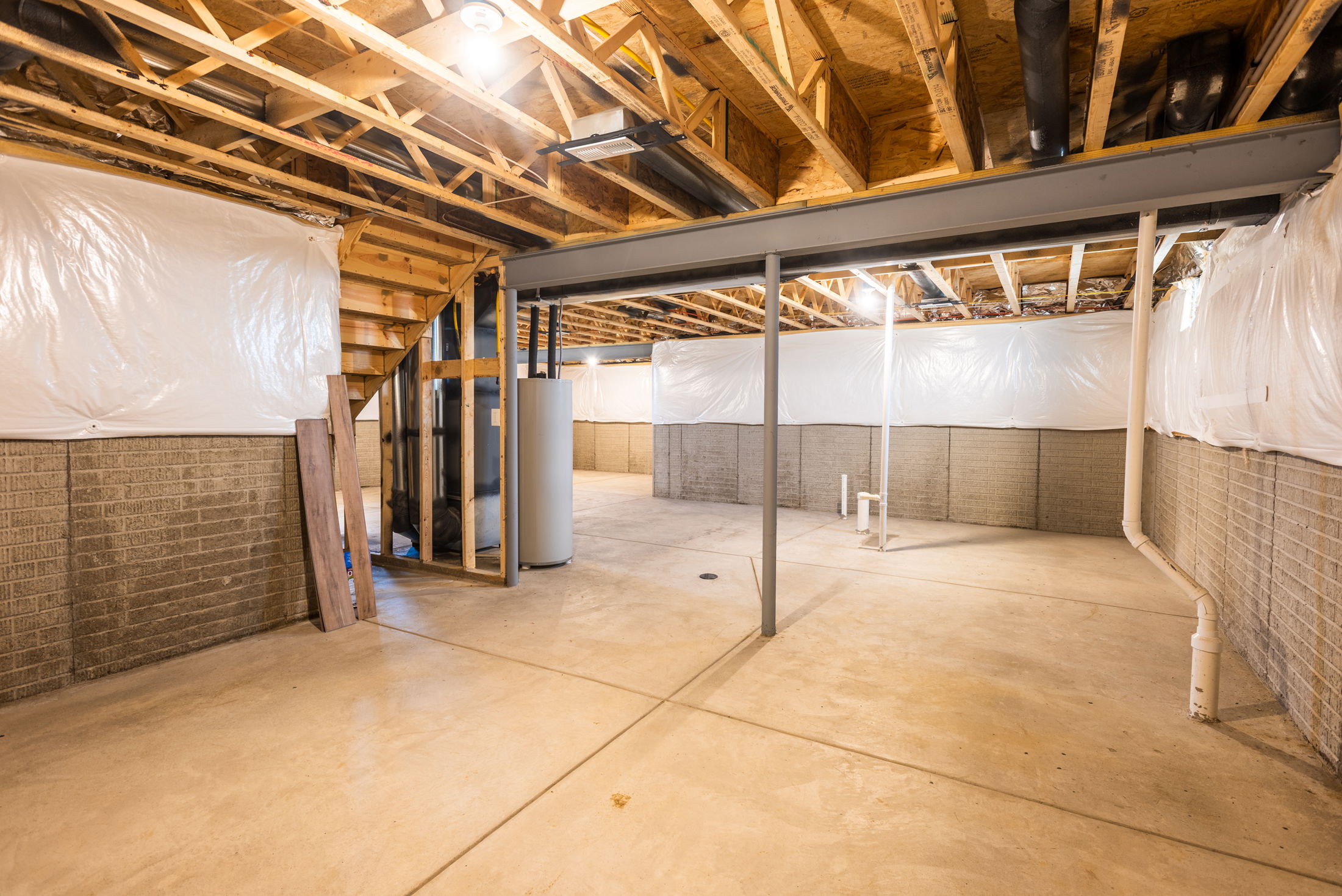 Unfinished basement with exposed wooden beams, concrete floor, brick walls, and a water heater.
