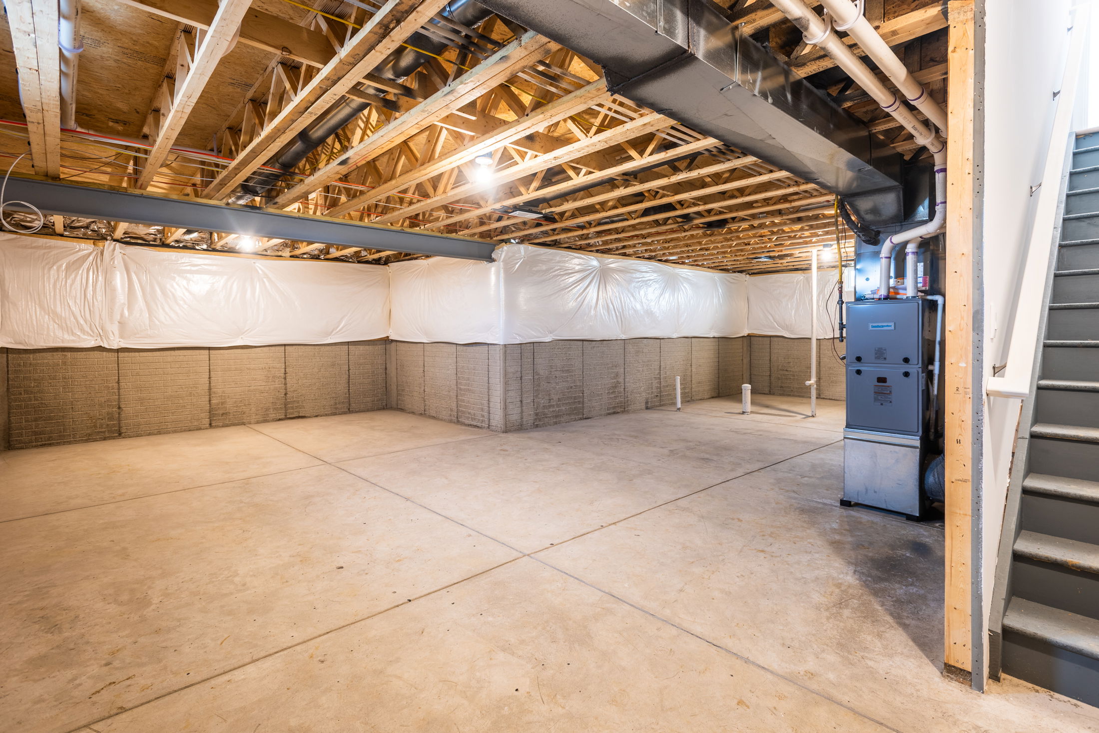 Spacious unfinished basement with concrete floors, exposed wooden beams, and a heating unit, ideal for renovation or storage.