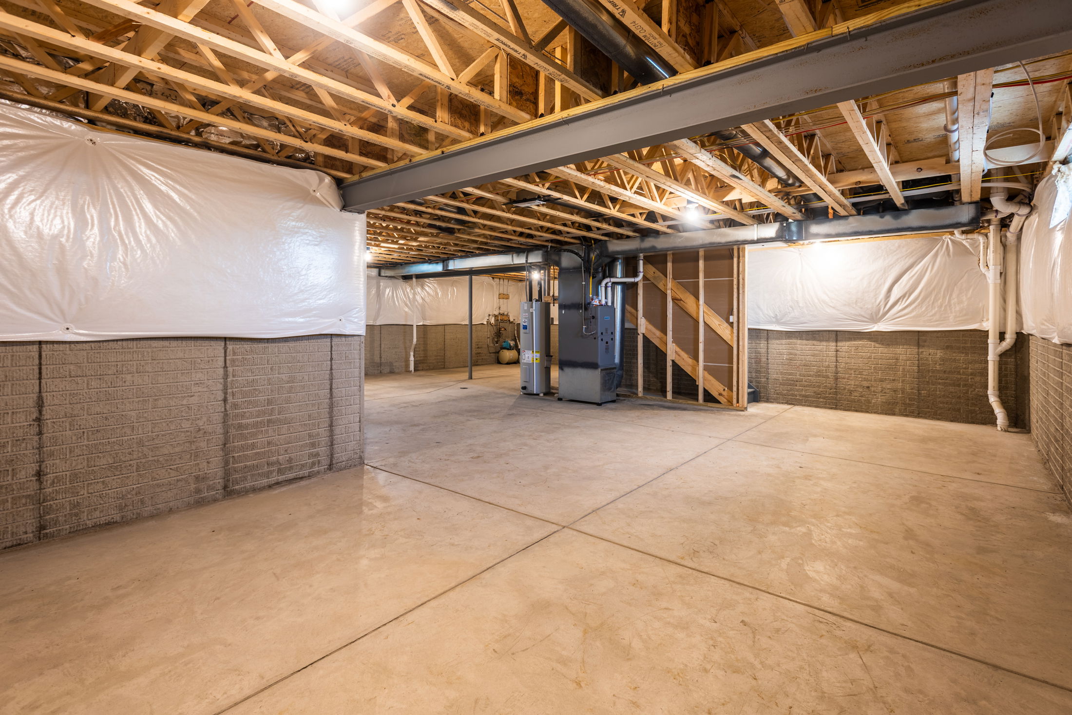 An unfinished basement with exposed wooden ceiling beams, concrete floors, and utility equipment.