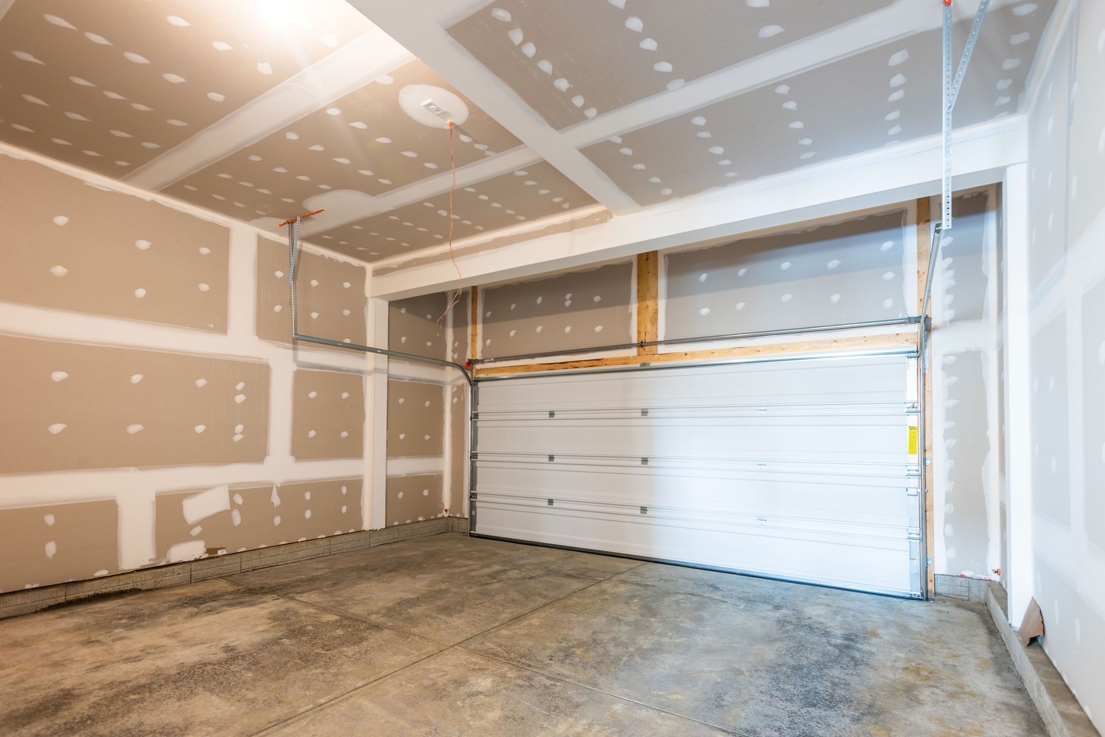 Empty garage interior with unfinished drywall and a closed white overhead door.