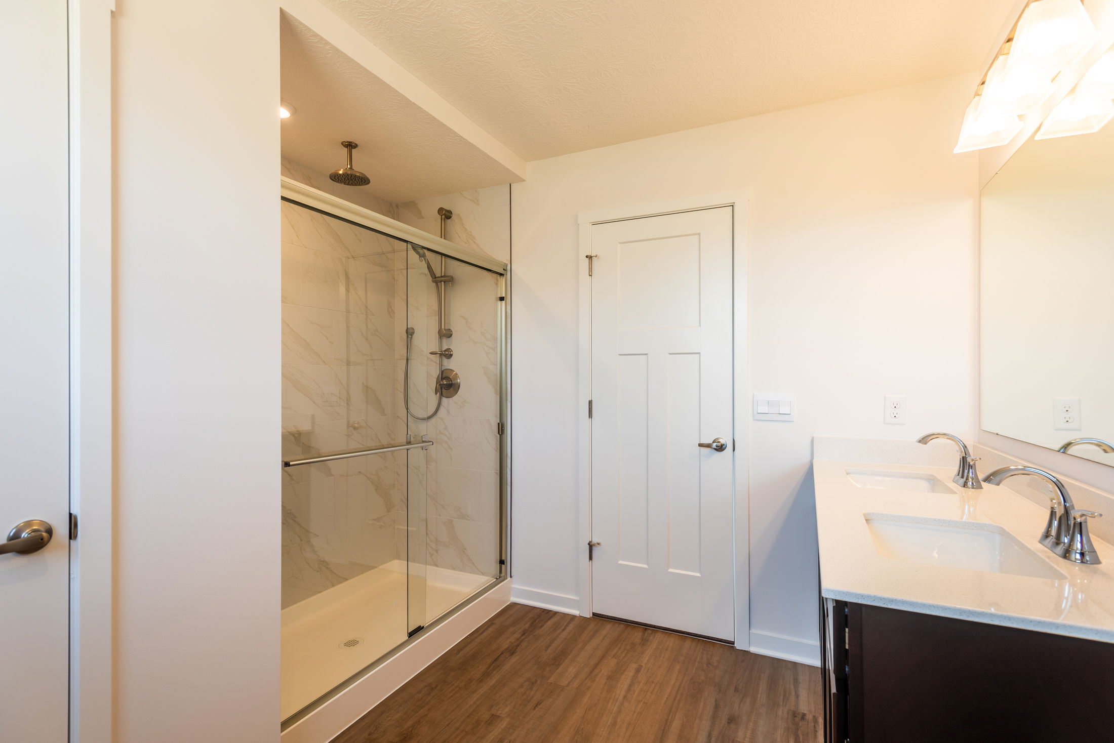 Modern bathroom interior featuring a glass-enclosed shower, dual sink vanity, and wood flooring.