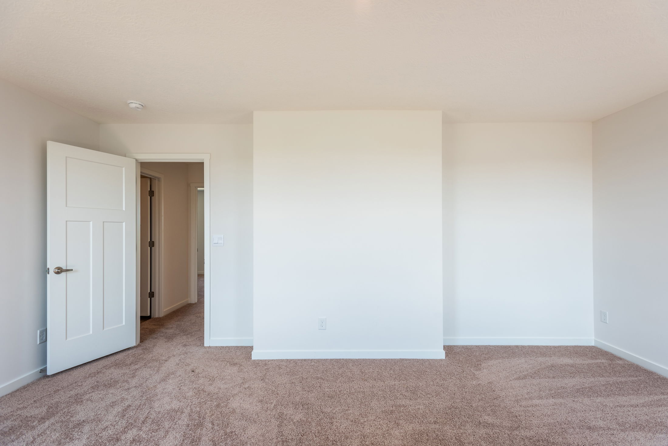 Empty room with beige carpet, white walls, and an open door leading to a hallway.