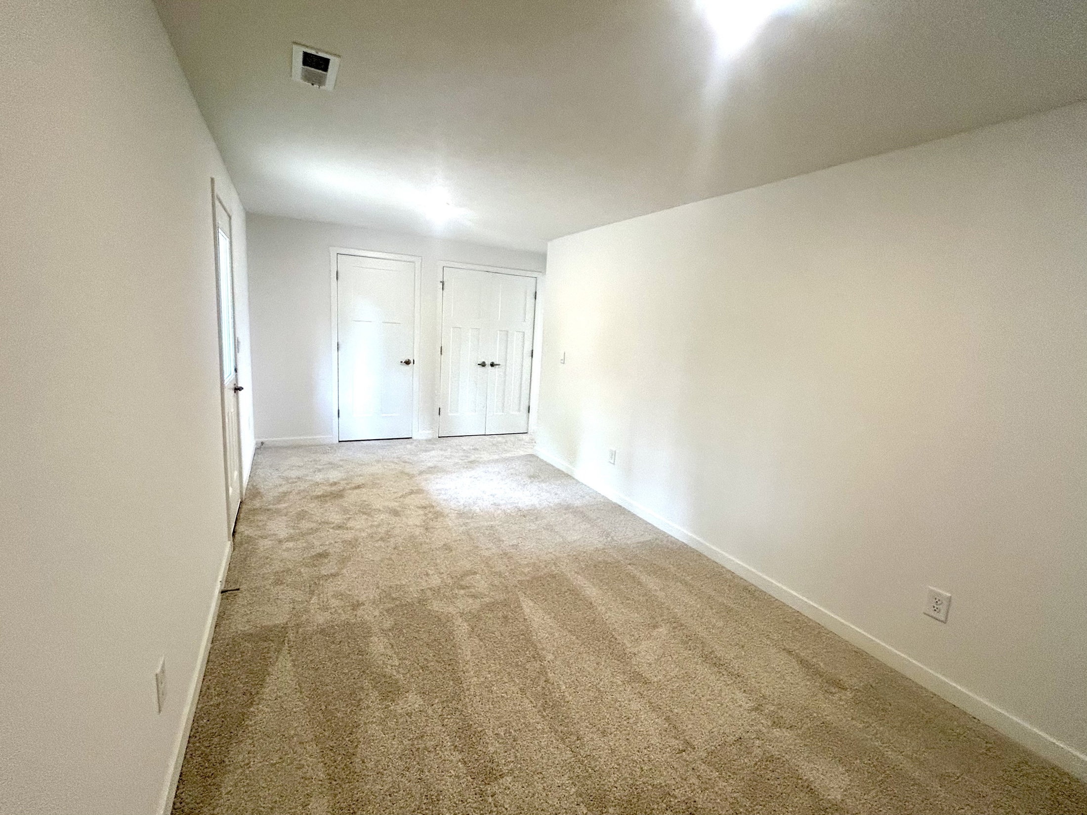 Spacious, empty room with beige carpet and two white doors leading to storage areas.
