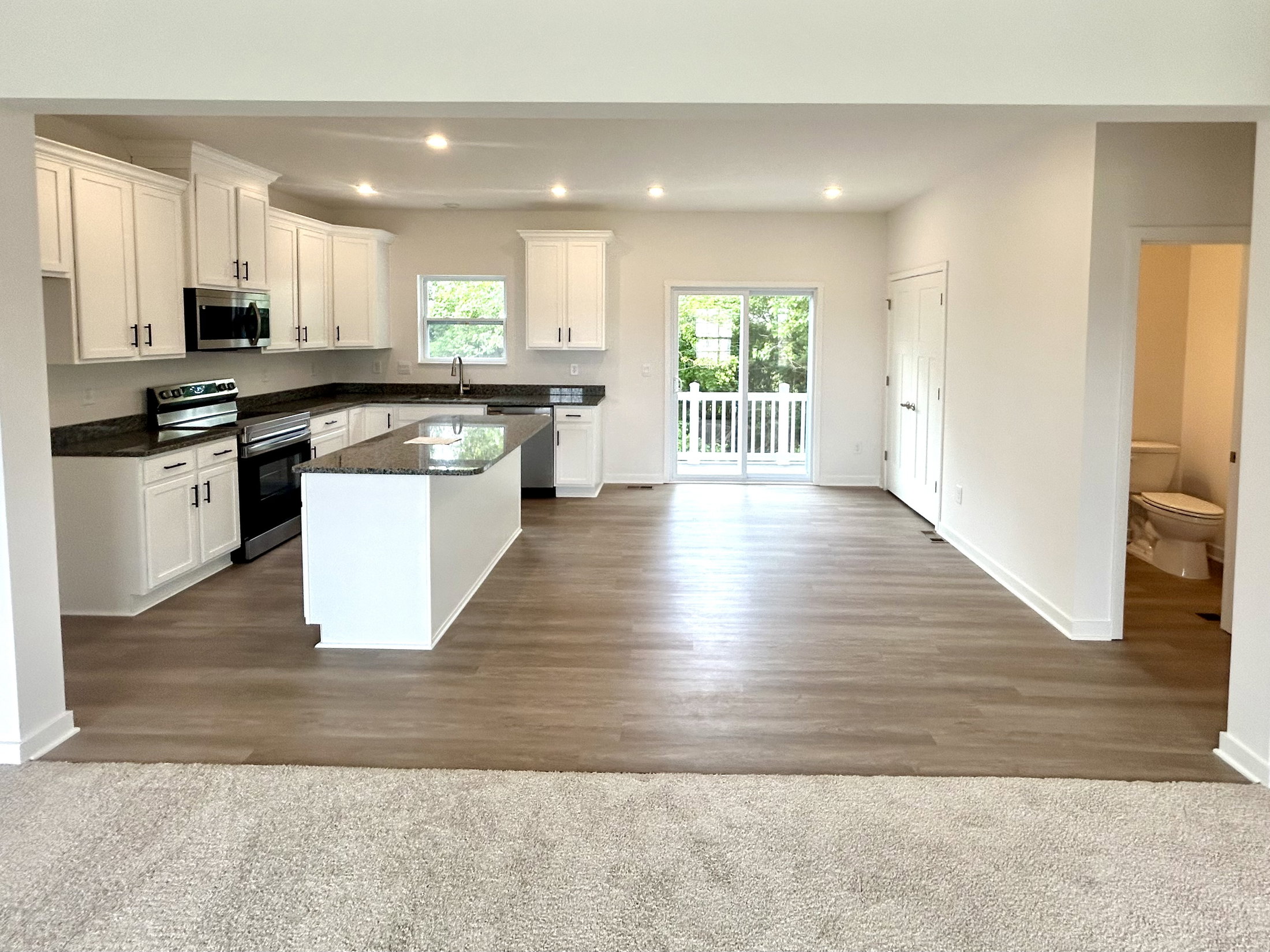 Modern open-concept kitchen and living area with white cabinets, stainless steel appliances, and hardwood floors.