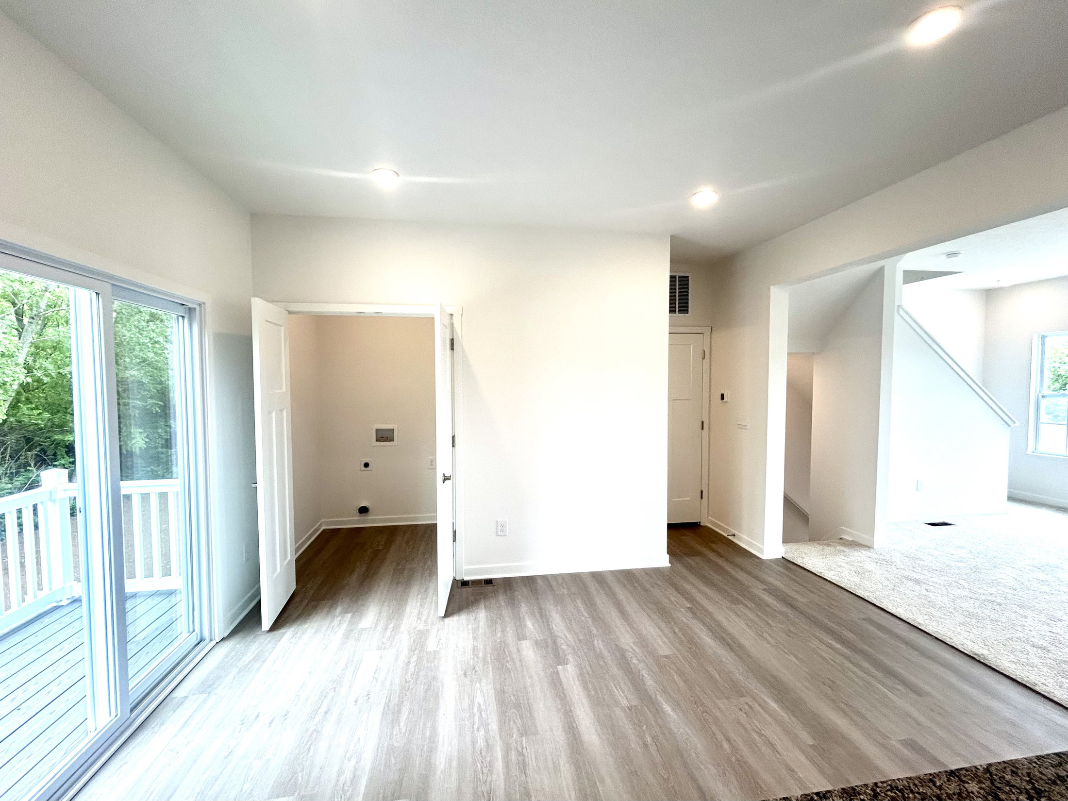 Modern interior of a bright, spacious living area featuring hardwood floors, open doorways, and natural light from large windows.