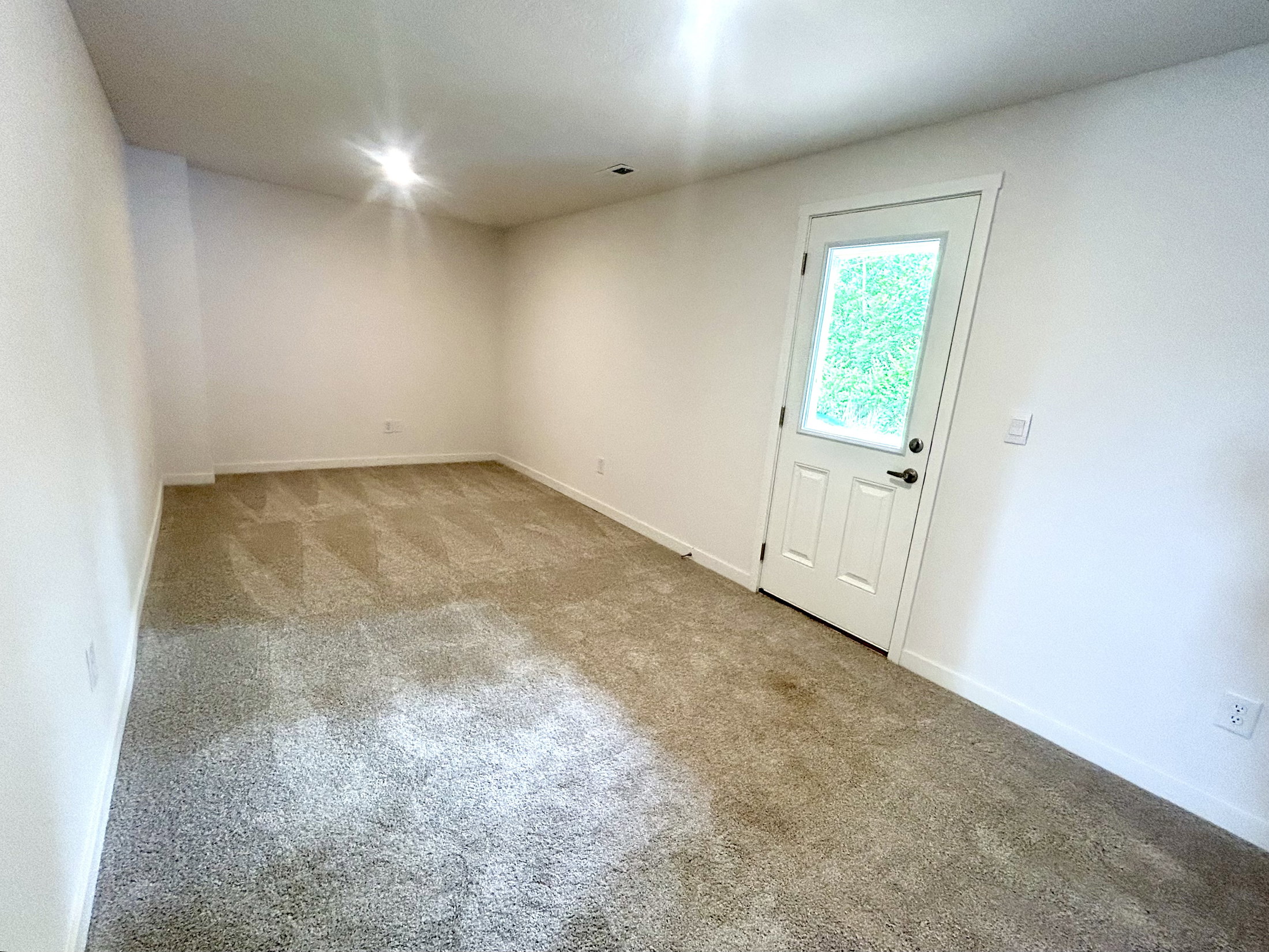 Cozy empty room with carpet flooring and a door leading to the outdoors, illuminated by soft ceiling lights.