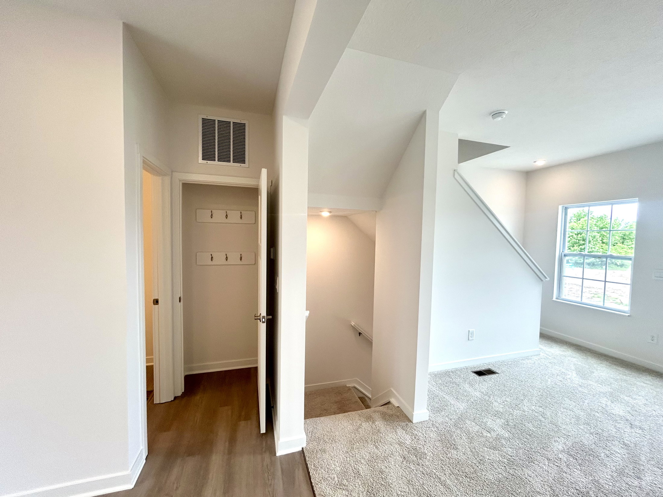 Bright and airy hallway featuring carpeted flooring, a window for natural light, and a staircase leading to the upper level.