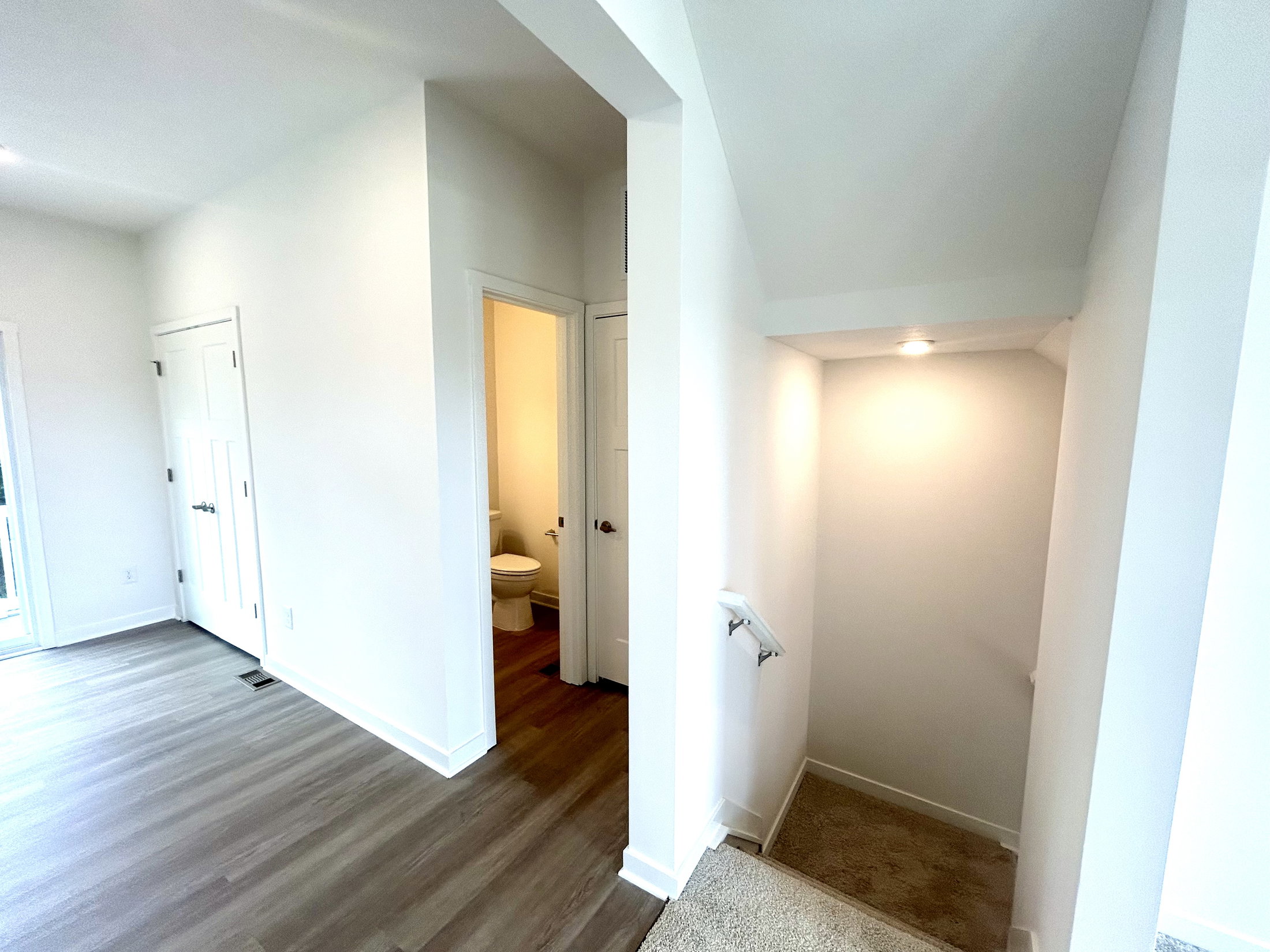 Bright and modern interior hallway with a staircase leading to a lower level and a doorway to a bathroom.