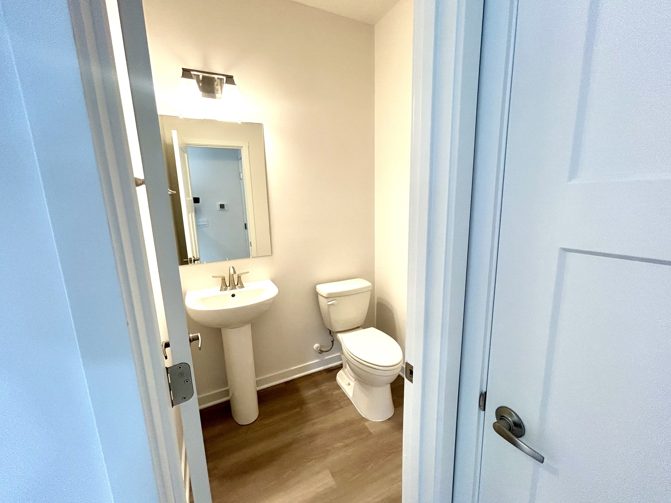 Modern bathroom featuring a pedestal sink, toilet, and a mirror, designed with neutral colors and contemporary lighting.