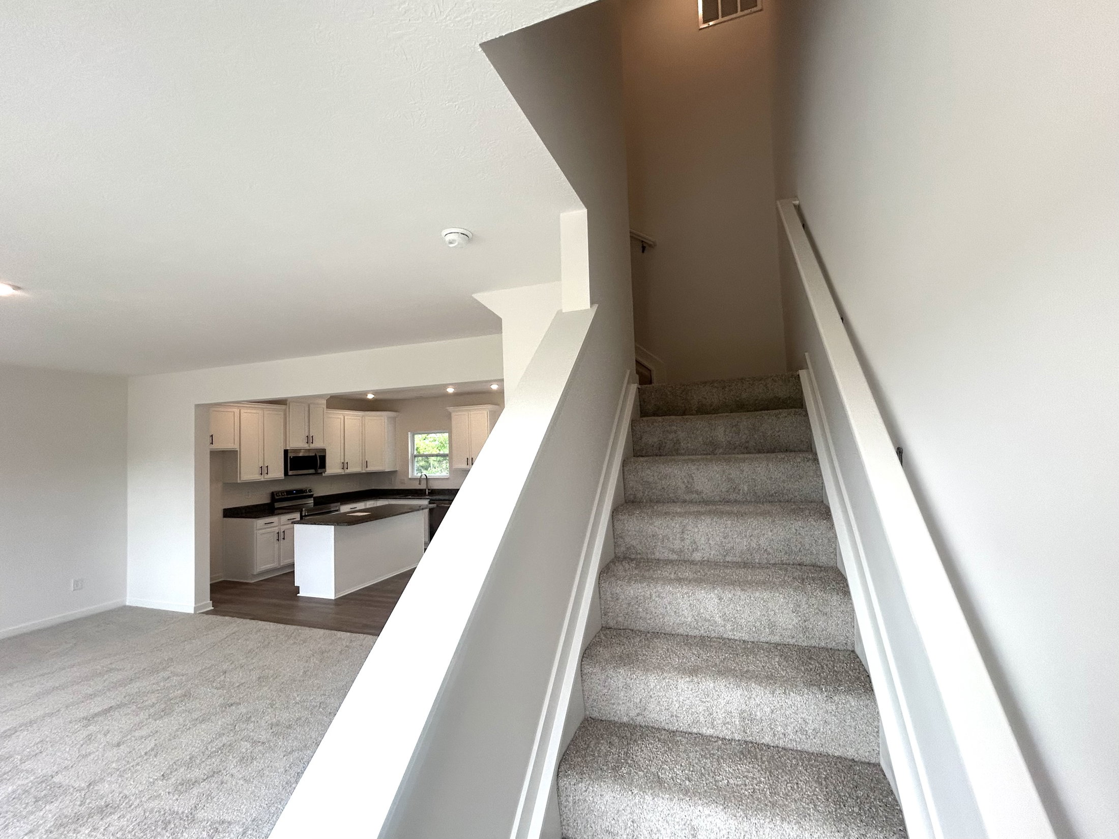 A bright and spacious interior view of a modern home featuring a staircase leading to the upper level, with a glance into the open-concept kitchen and living area.